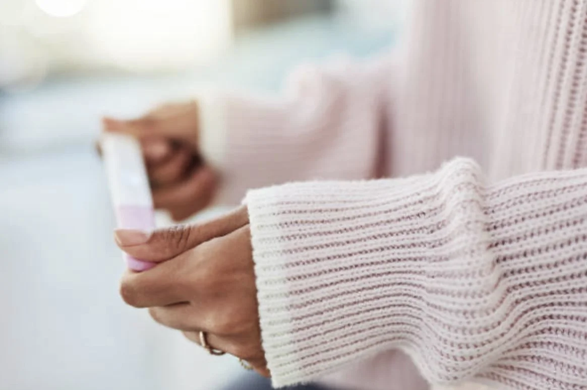 Person holding a pink smartphone, wearing a white knitted sweater with pink stripes.