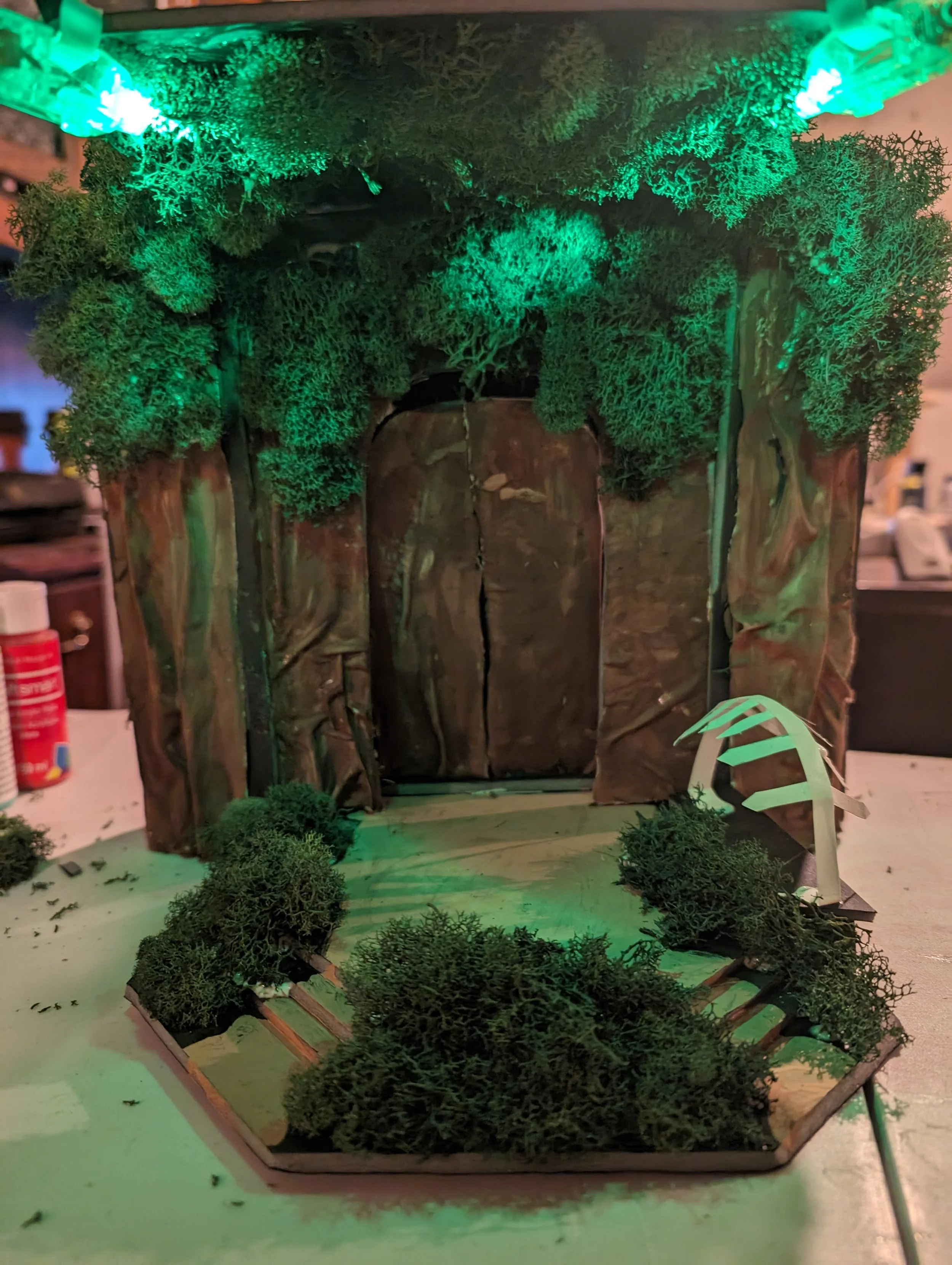 Model for The Tempest
To engulf the audience in the tropical environment of The Tempest, shrubbery is positioned around the acting area as well as the ceiling.  The back wall is decorated with tree decal to blend in with the shrubbery as well. In add