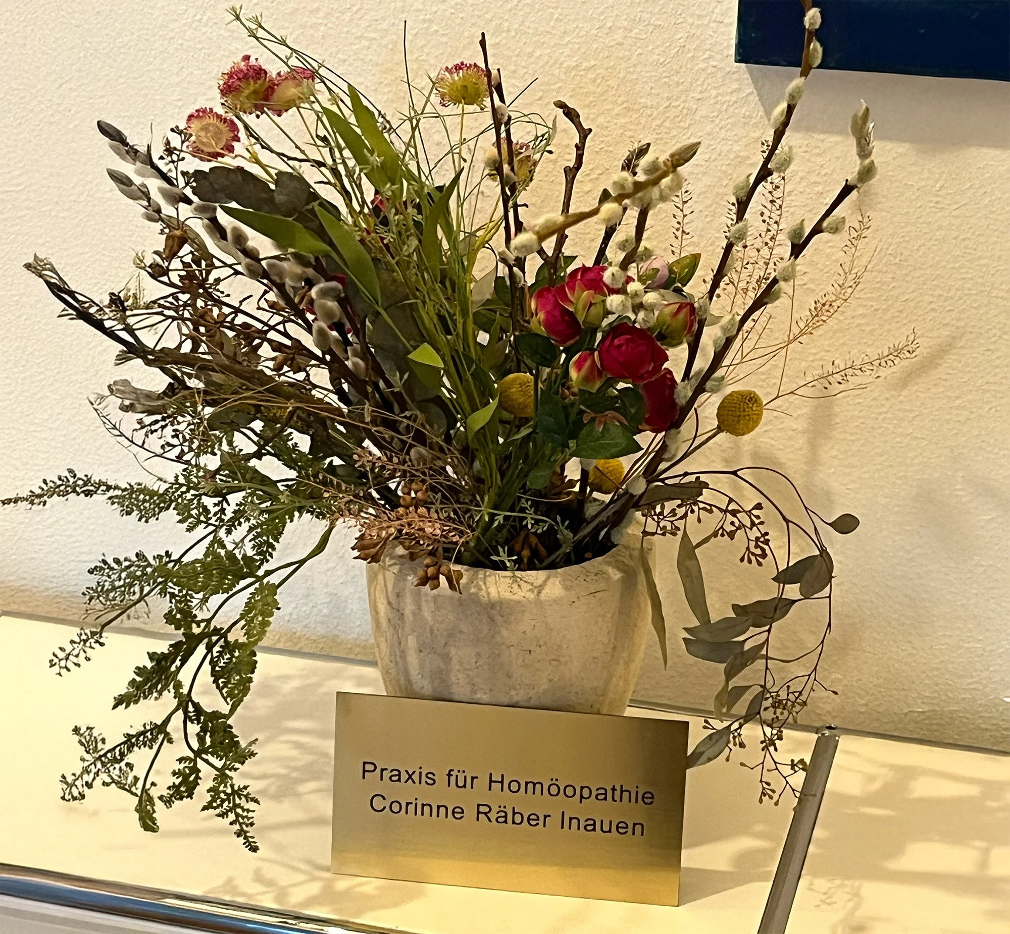 Blumenstrauß in einer Schüssel mit einem Schild, das 'Praxis für Homöopathie Corinne Raber Inauen' sagt.