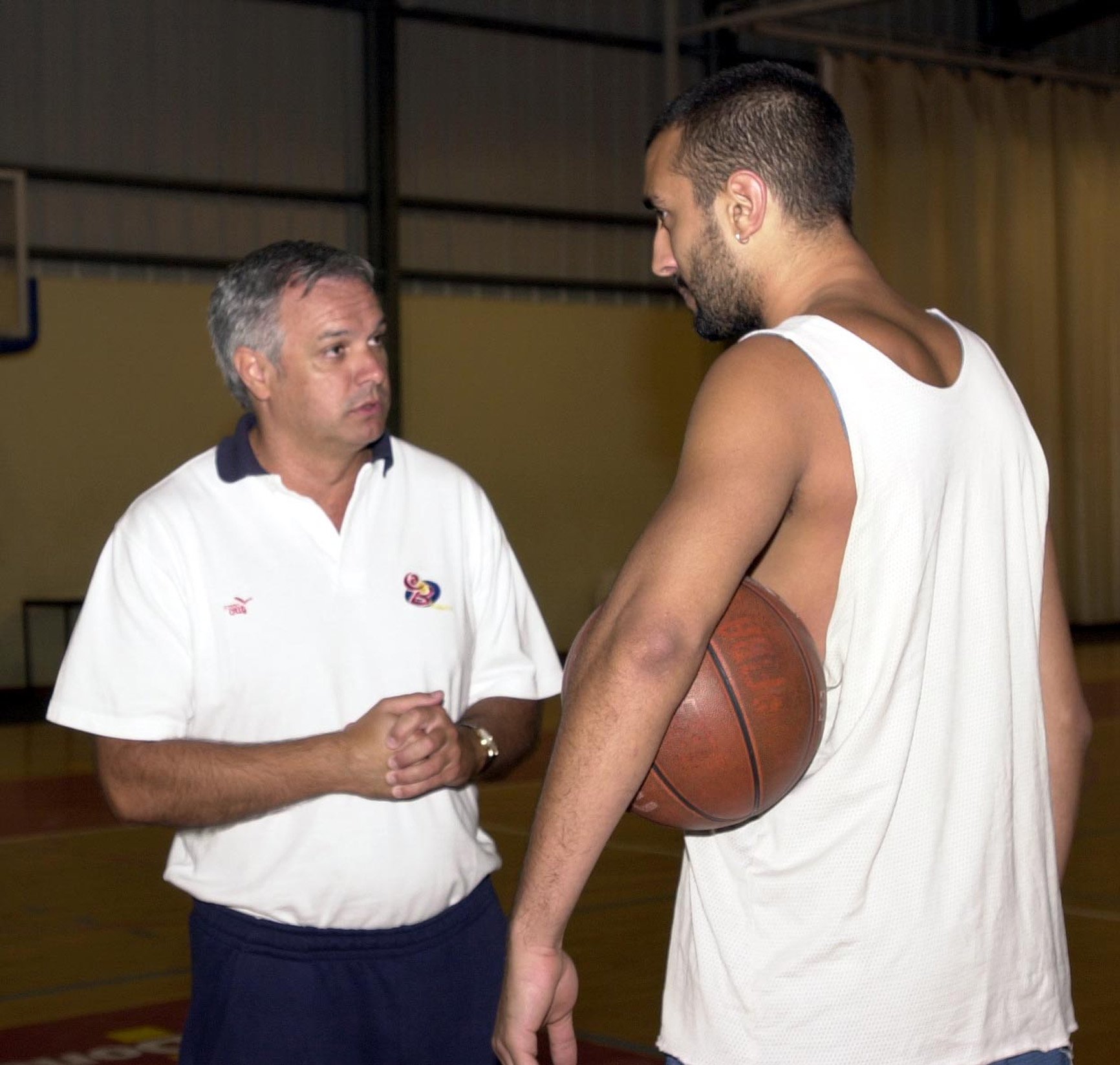 A basketball coach speaking to a player holding a basketball in a gymnasium.