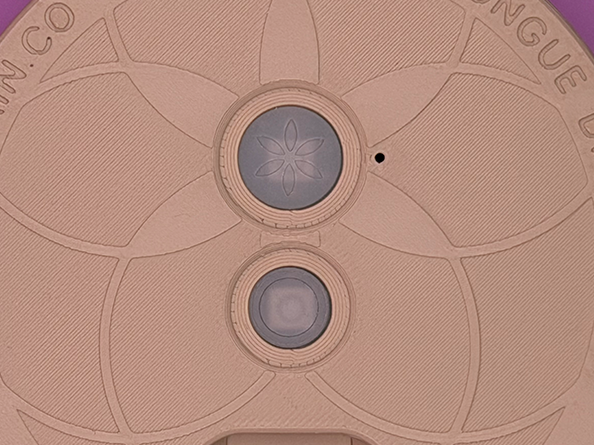 Close-up of a beige or light-colored device with circular and segmented patterns, featuring two central circular components and a small black dot on the right side.