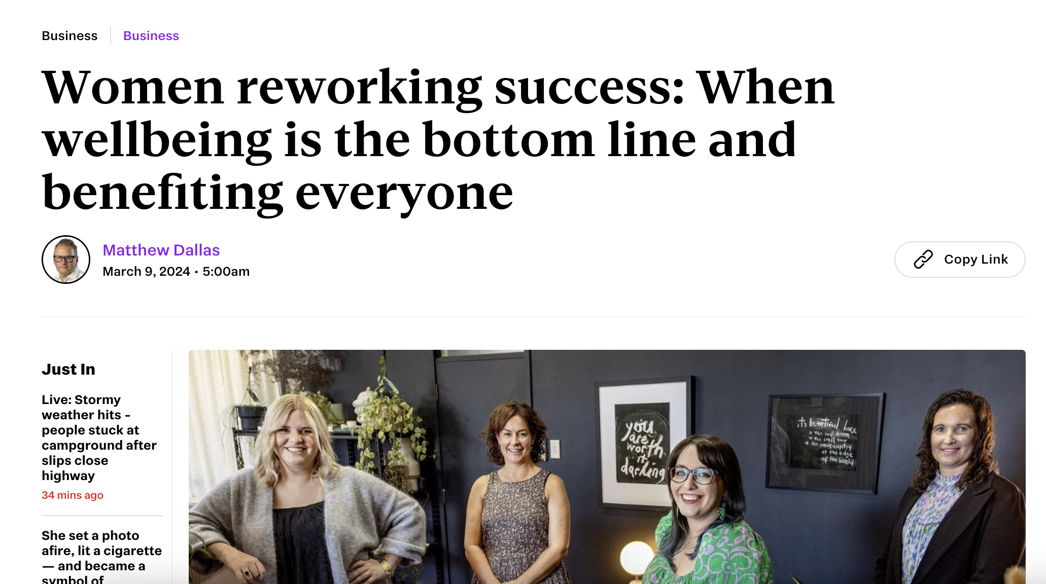 Group of four women standing indoors, smiling, with framed artwork and plants in the background.