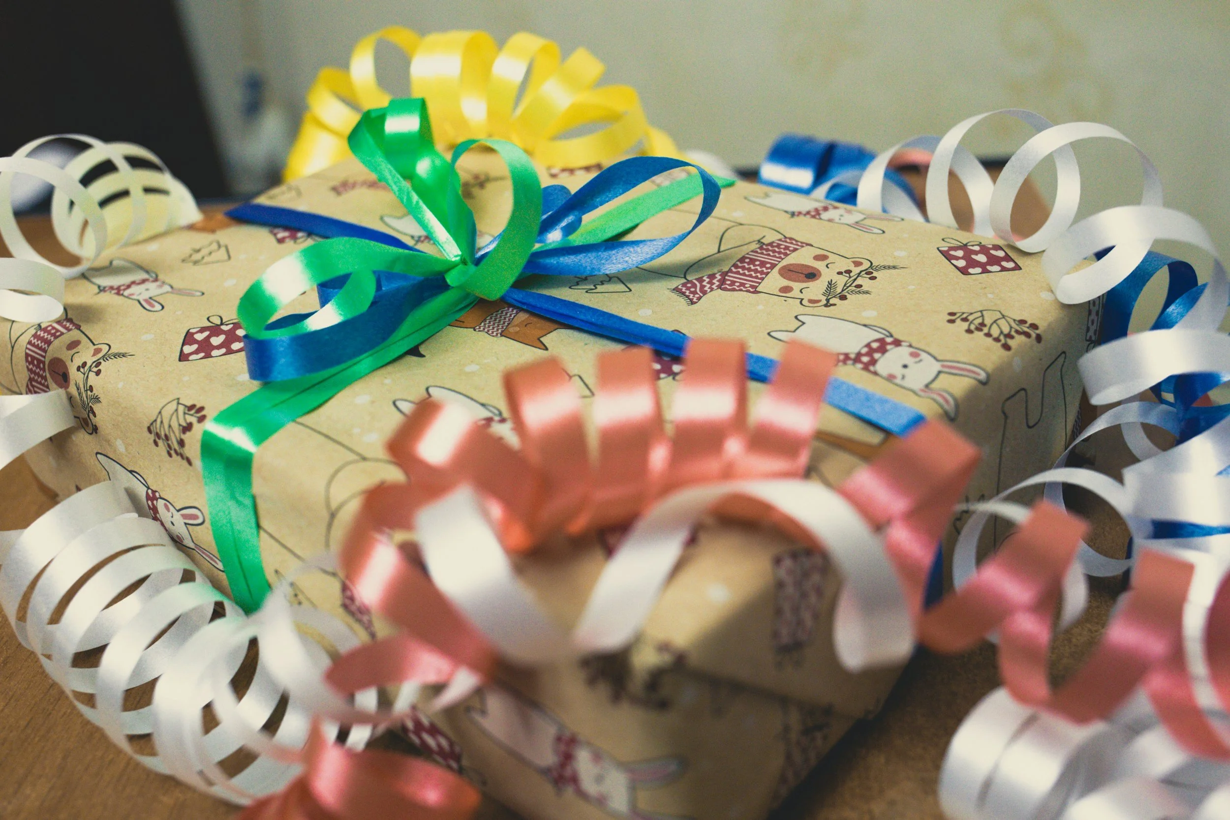 Wrapped gift box with holiday-themed paper, decorated with colorful ribbons and curled paper streamers.