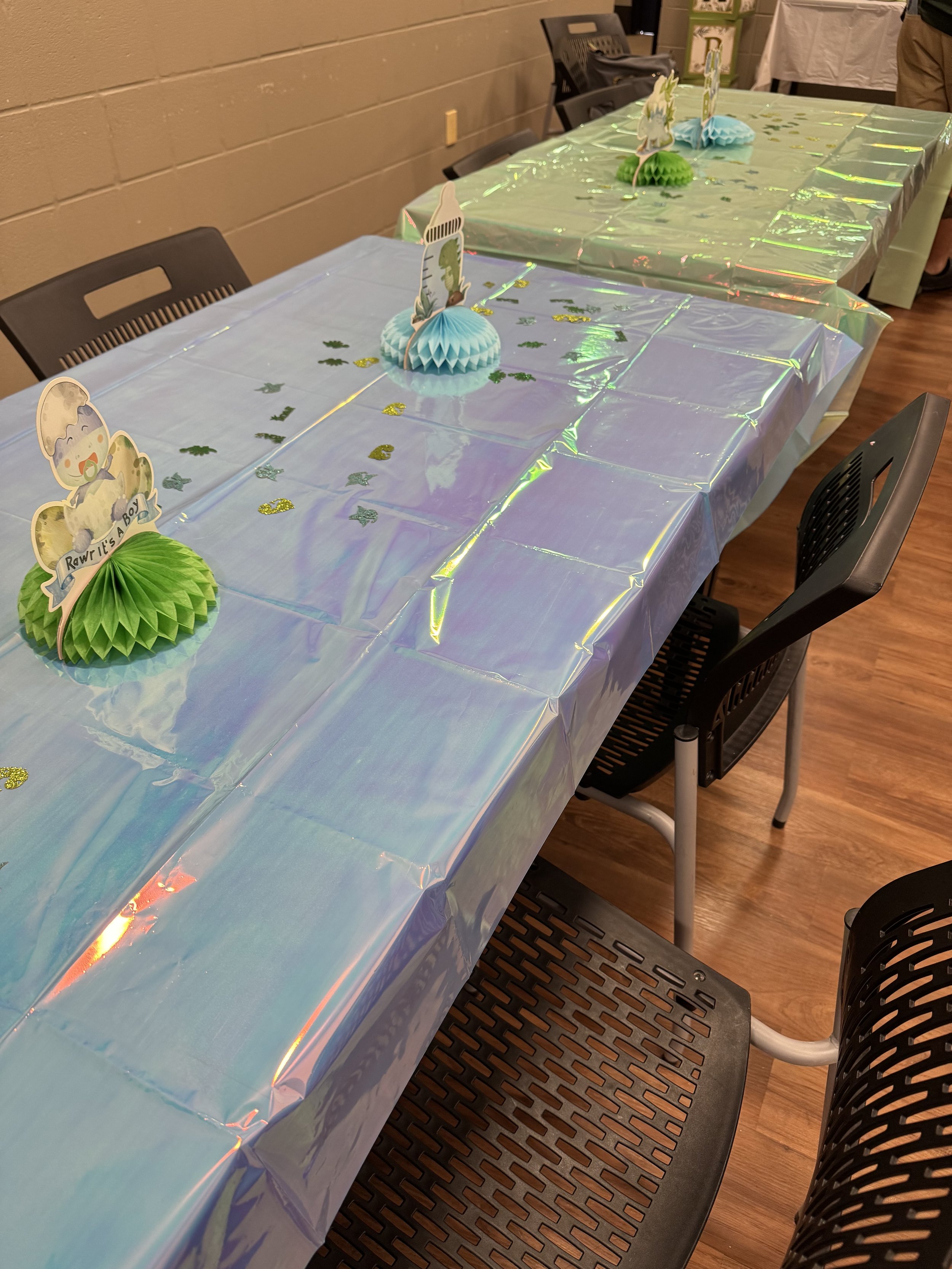 Decorated tables with pastel blue and green party favors, cupcakes, and dinosaur themed toppers for a celebration in an indoor setting.