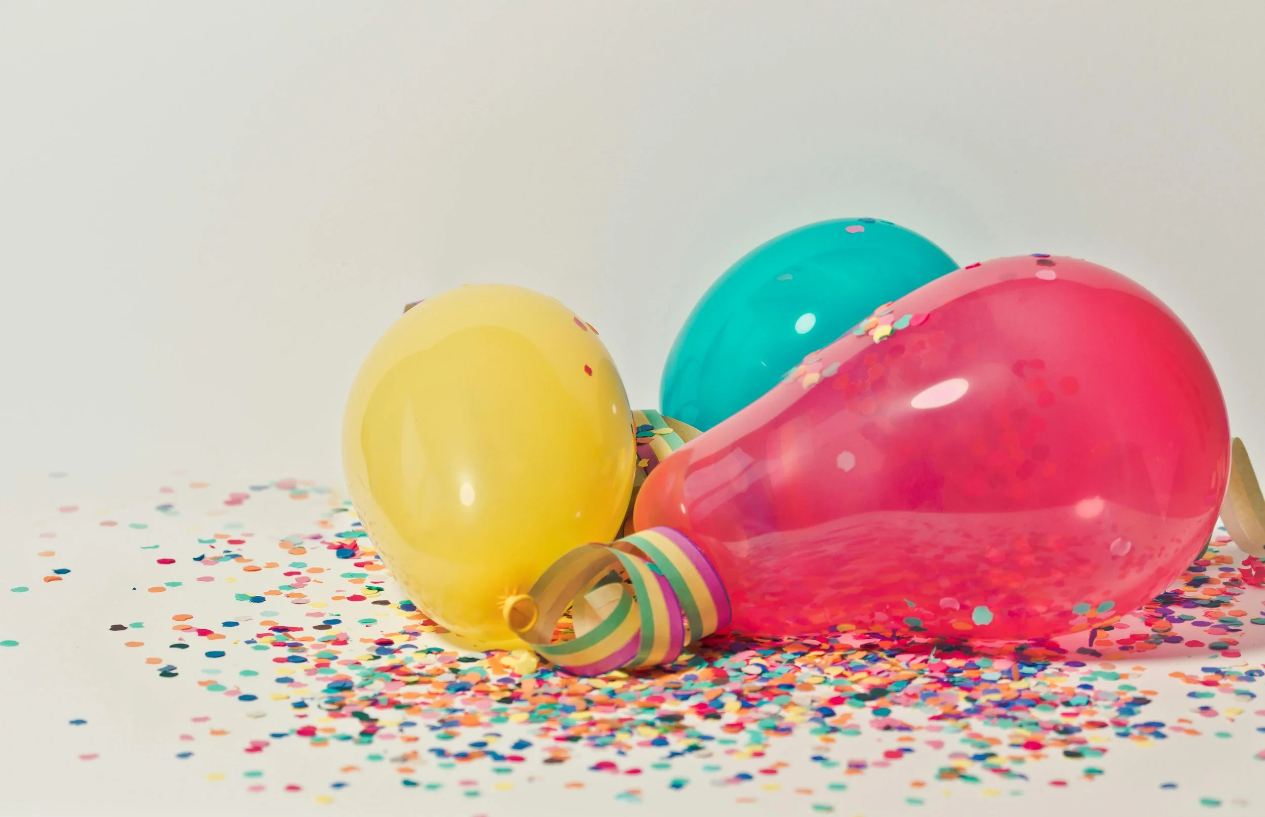 Colorful balloons and confetti on a white background for celebration.