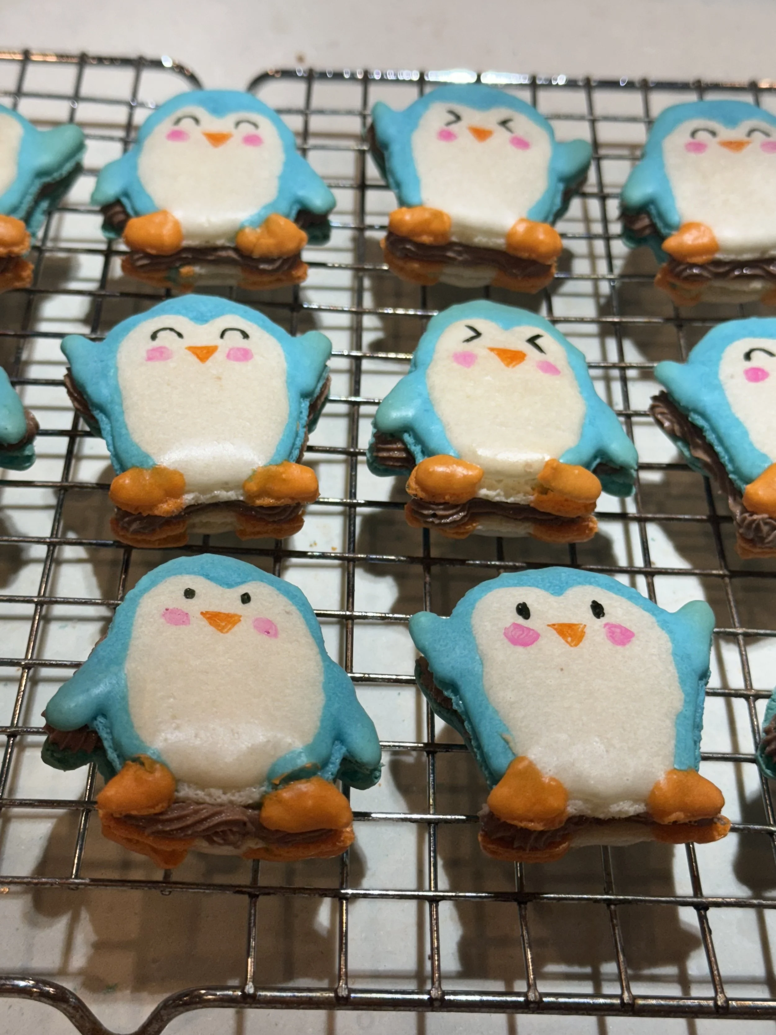 Penguin-shaped cookies decorated with blue, white, orange, and black icing on a cooling rack.