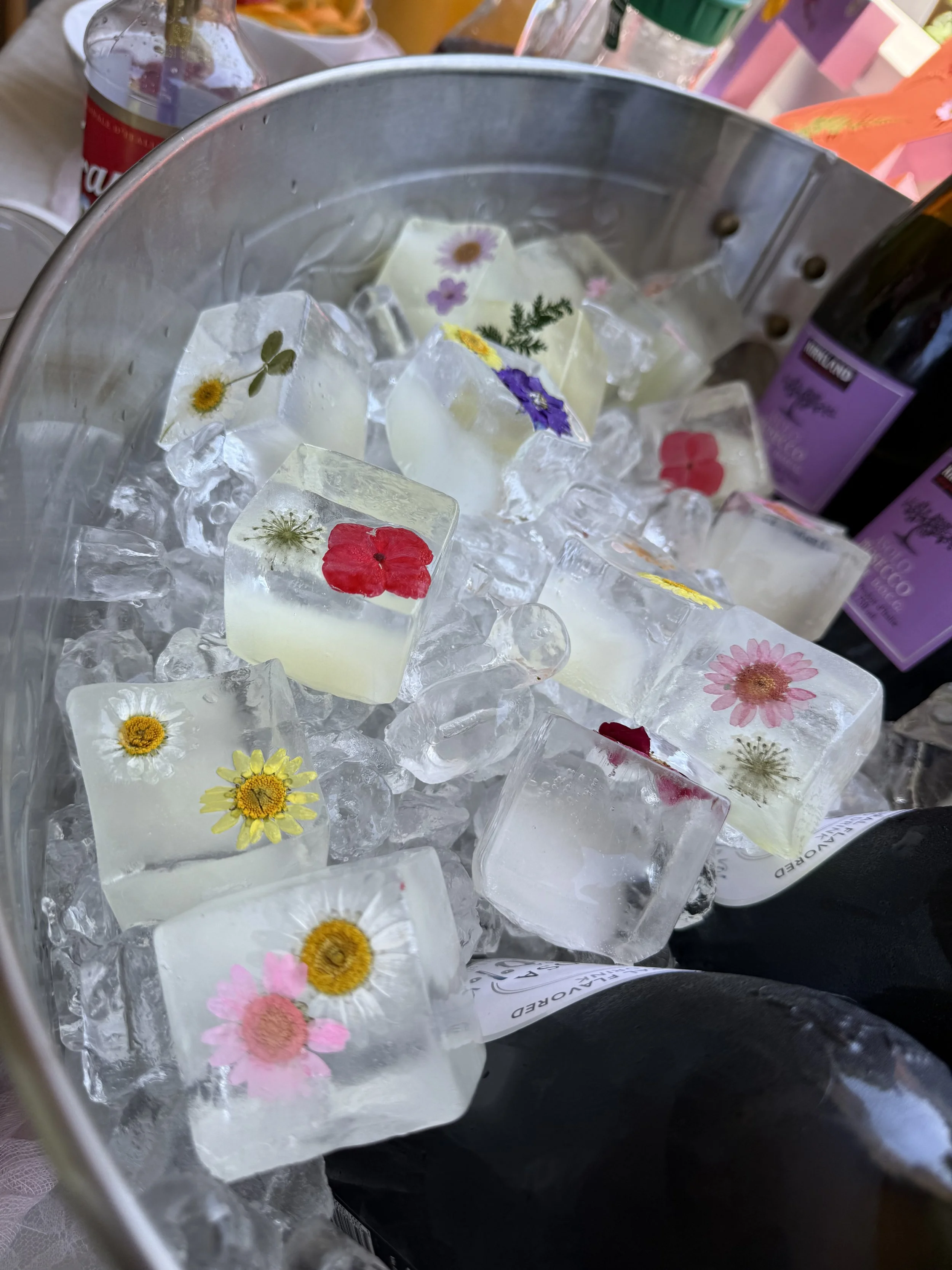 Ice cubes with pressed flowers such as daisies and poppies inside, in a metal bucket.
