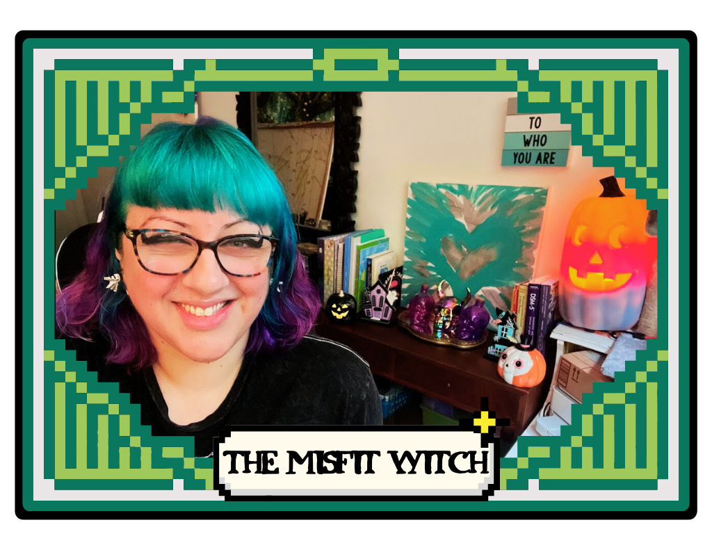 A woman/nonbinary person with teal and purple hair smiling in a room decorated with Halloween and witch-themed items, including pumpkins, skulls, and a sign that says 'BE TRUE TO WHO YOU ARE'.
