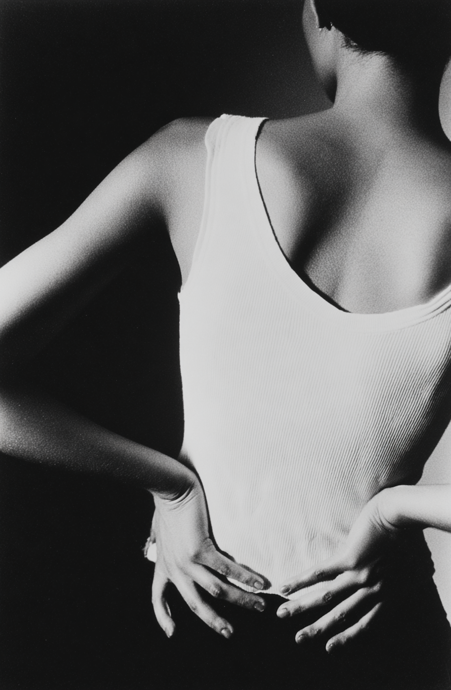 Black and white photograph of a woman from the shoulders down, wearing a sleeveless top, with her hands resting on her hips.