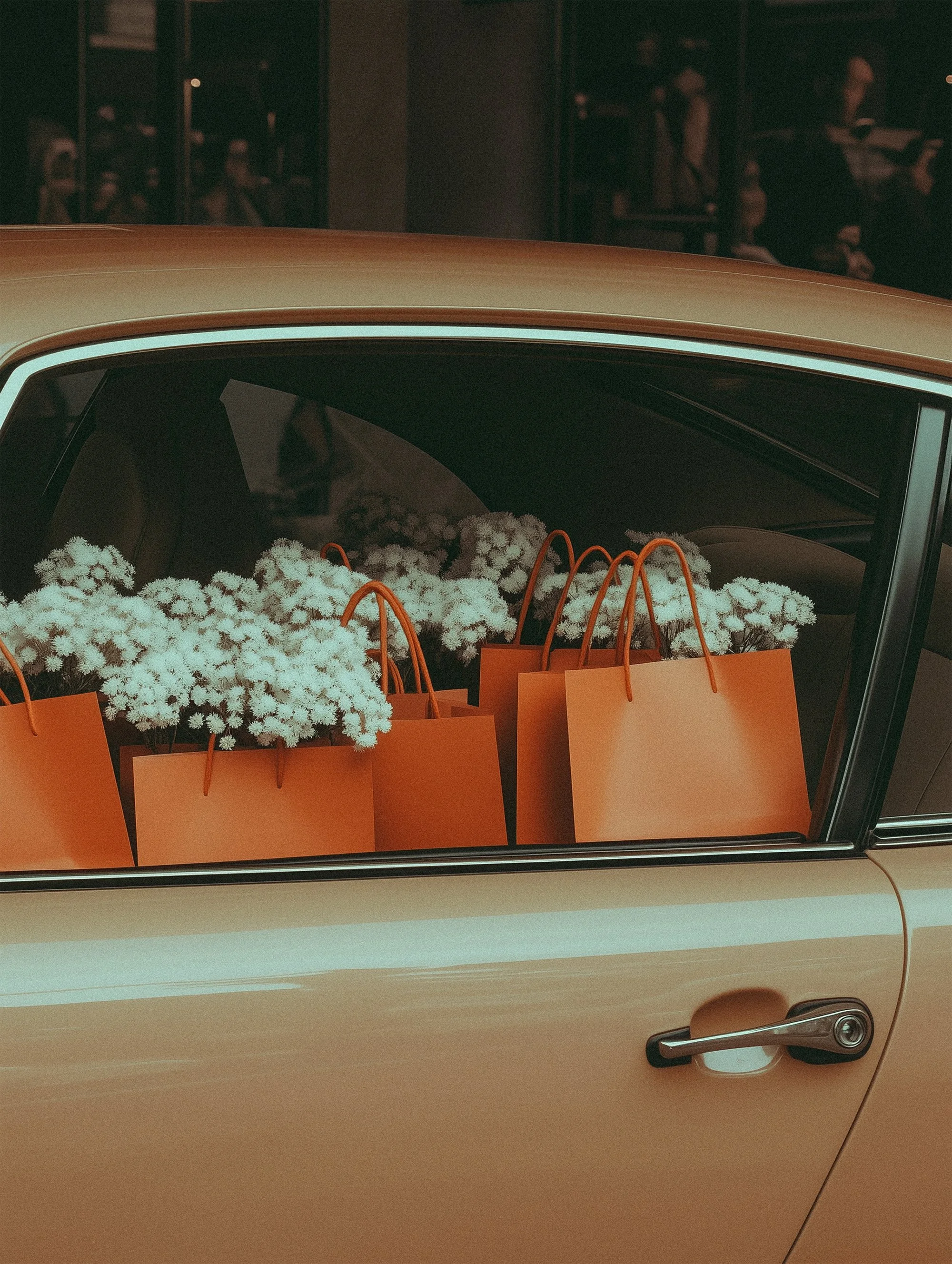 Orange shopping bags filled with white flowers inside an open car window.