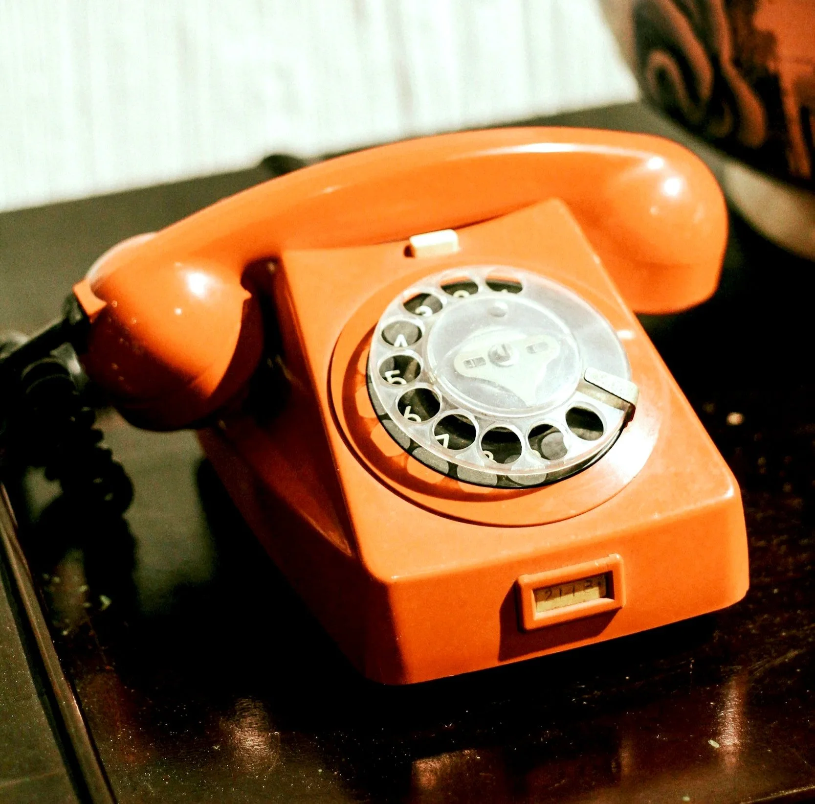 An orange rotary dial telephone placed on a dark wooden surface.