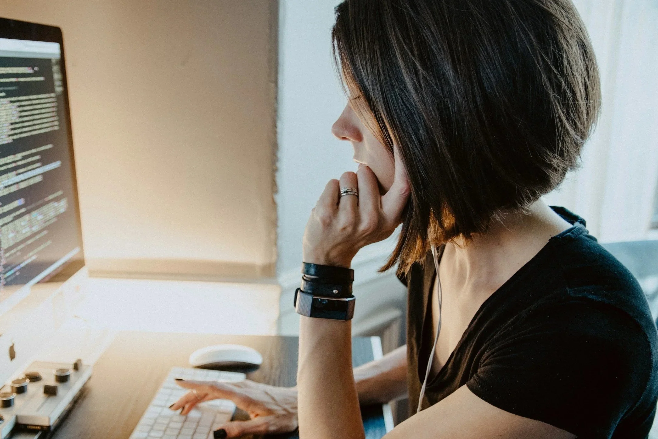 A woman with short dark hair working on a computer, with her hand on her chin and wearing a black shirt, sitting at a desk working on college level mathematics.
