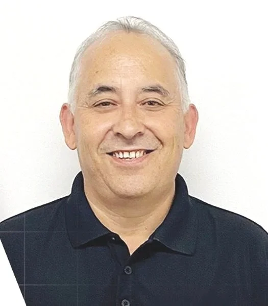 Portrait of a middle-aged man with gray hair, smiling, wearing a black collared shirt, against a plain white background.