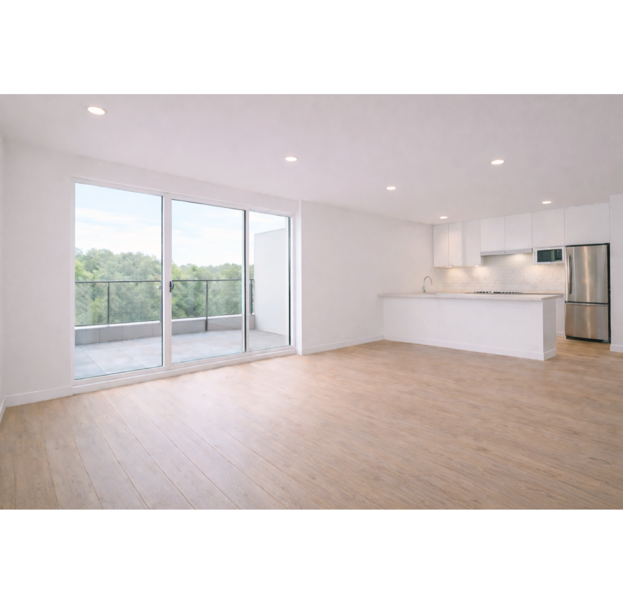 Intérieur d'une cuisine moderne avec des murs blancs, un plafond avec des spots lumineux, une grande fenêtre donnant sur un balcon, et un sol en bois clair.
