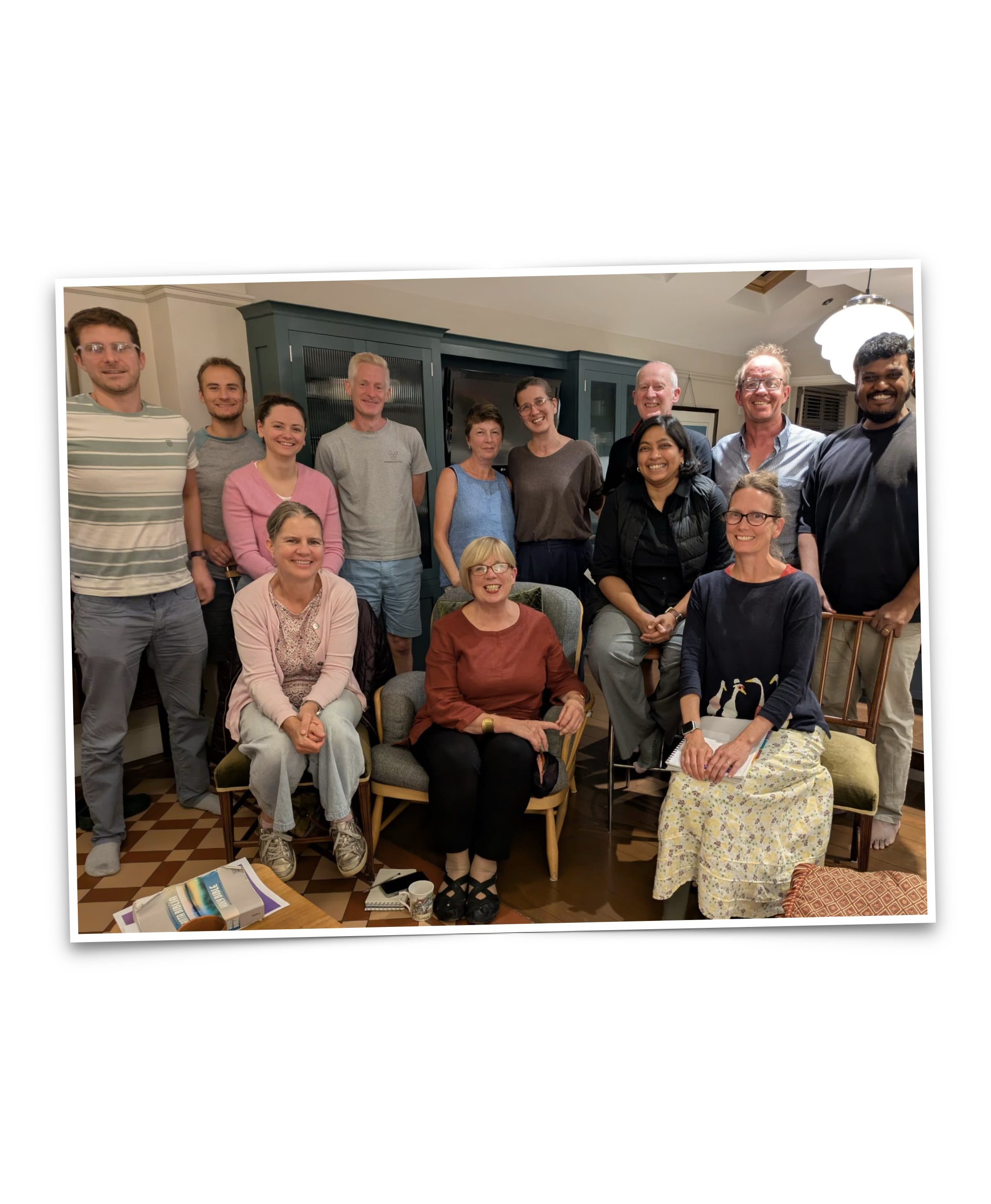 Group of 13 people gathered in a living room for a photo, some seated and some standing behind, smiling at the camera.