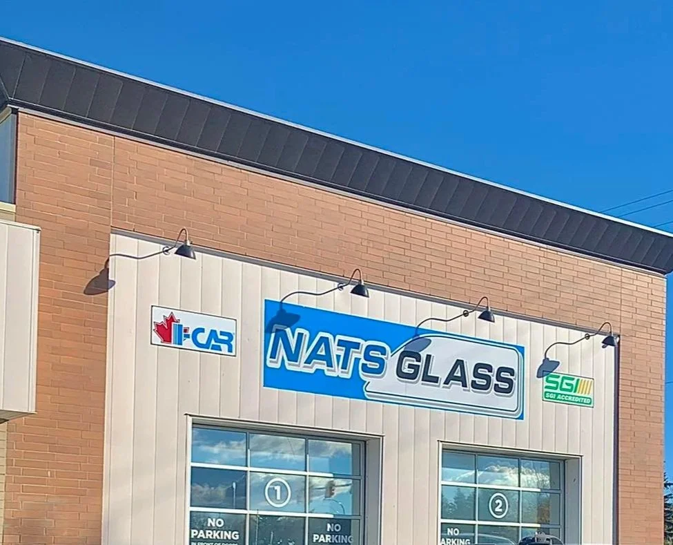 The exterior of Nats Glass store with signage and two large glass windows, under a clear blue sky.