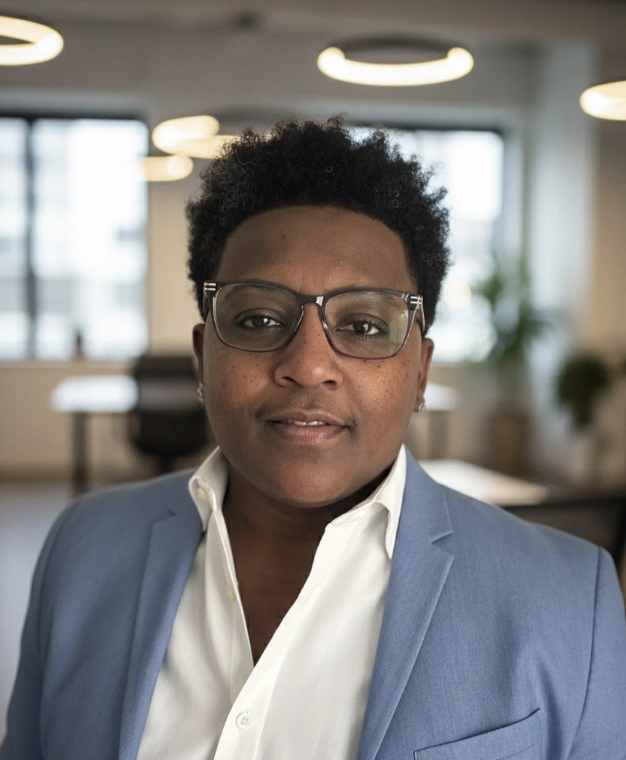 A professional woman with glasses wearing a blue blazer and white shirt in an office setting.