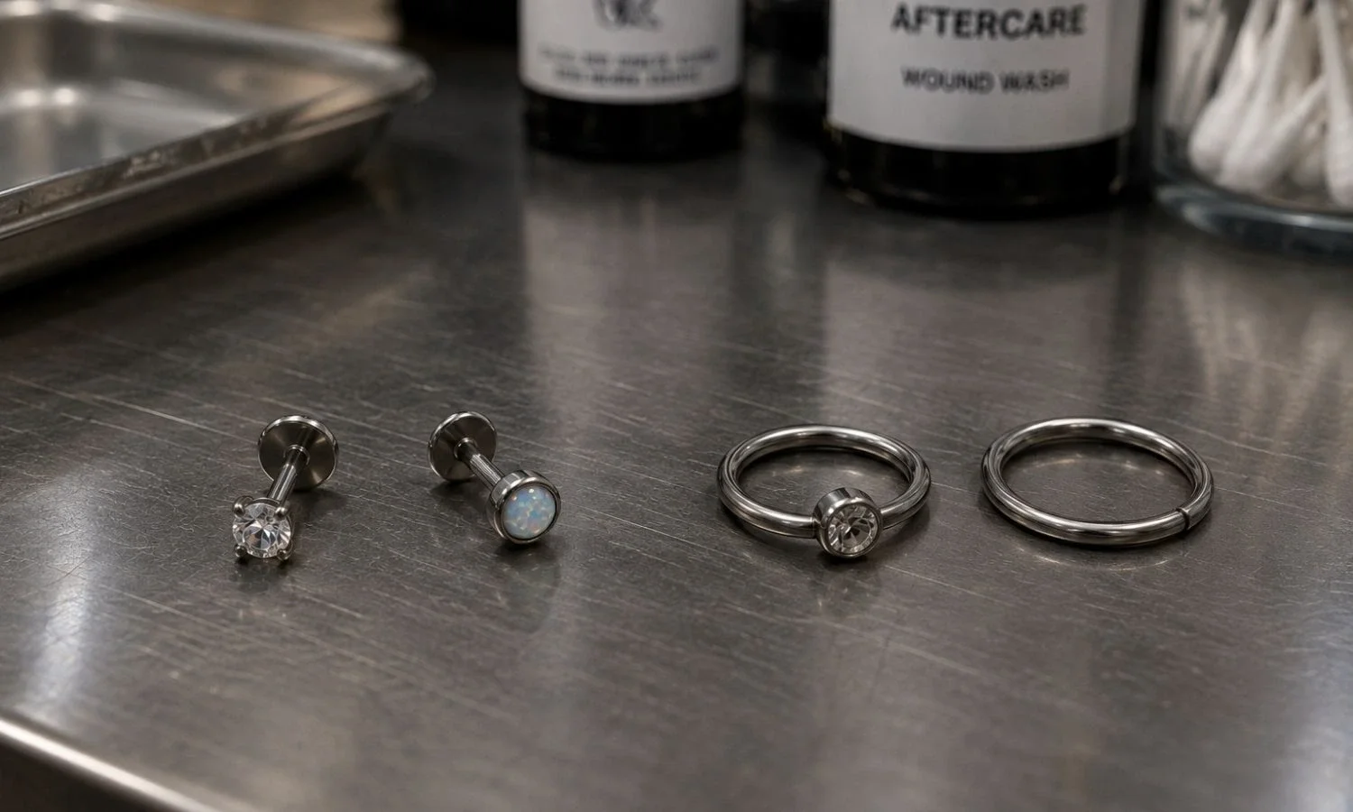 Flat-back studs and circular rings arranged on a sterile metal tray in a professional piercing studio