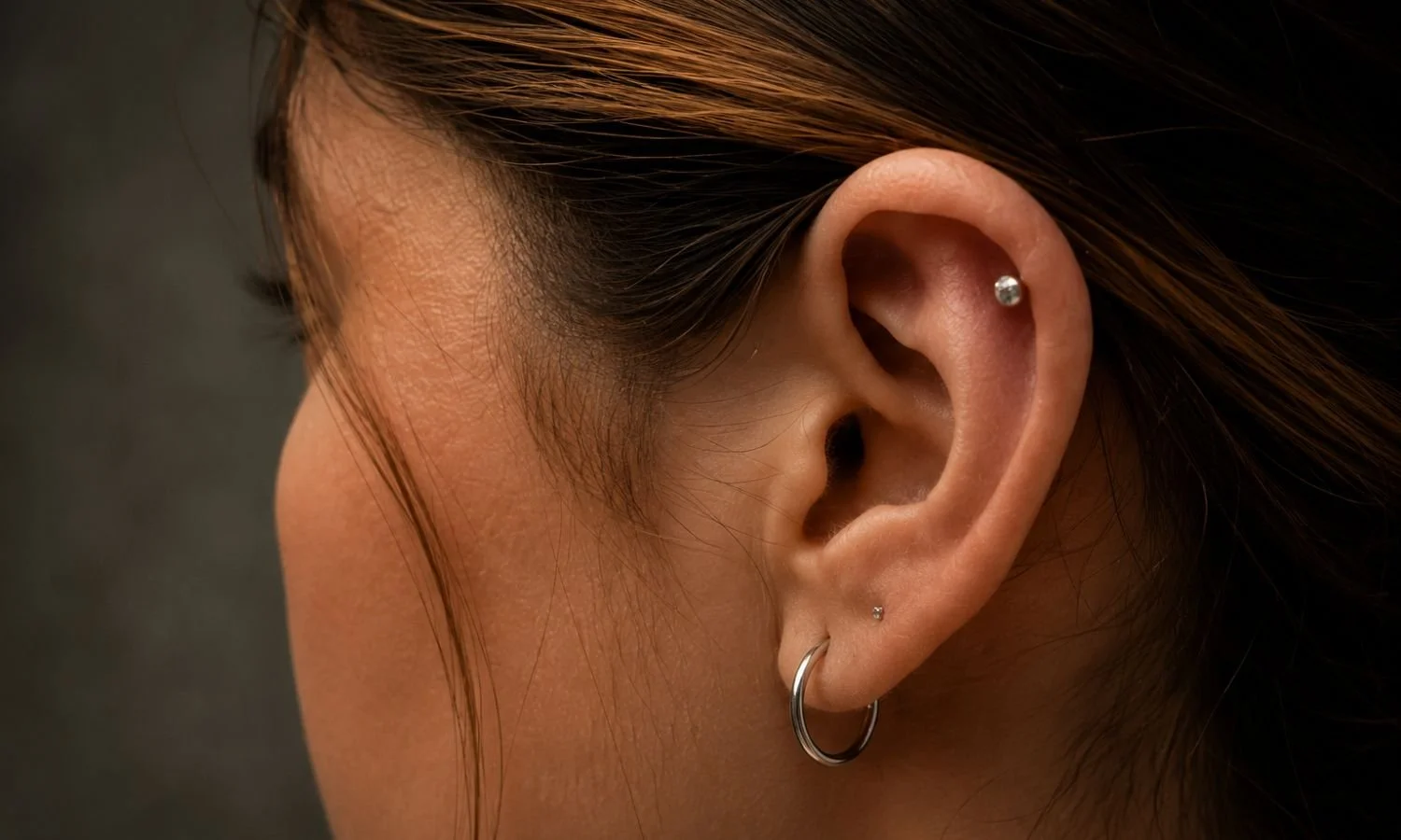 Helix cartilage piercing paired with lobe jewelry in a clean and minimalist ear curation style.