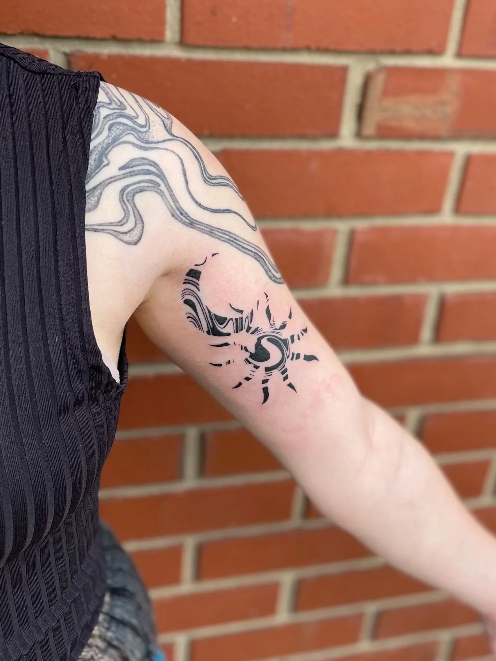 Tattoo of a crab with a swirling design on the upper arm against a brick wall background.