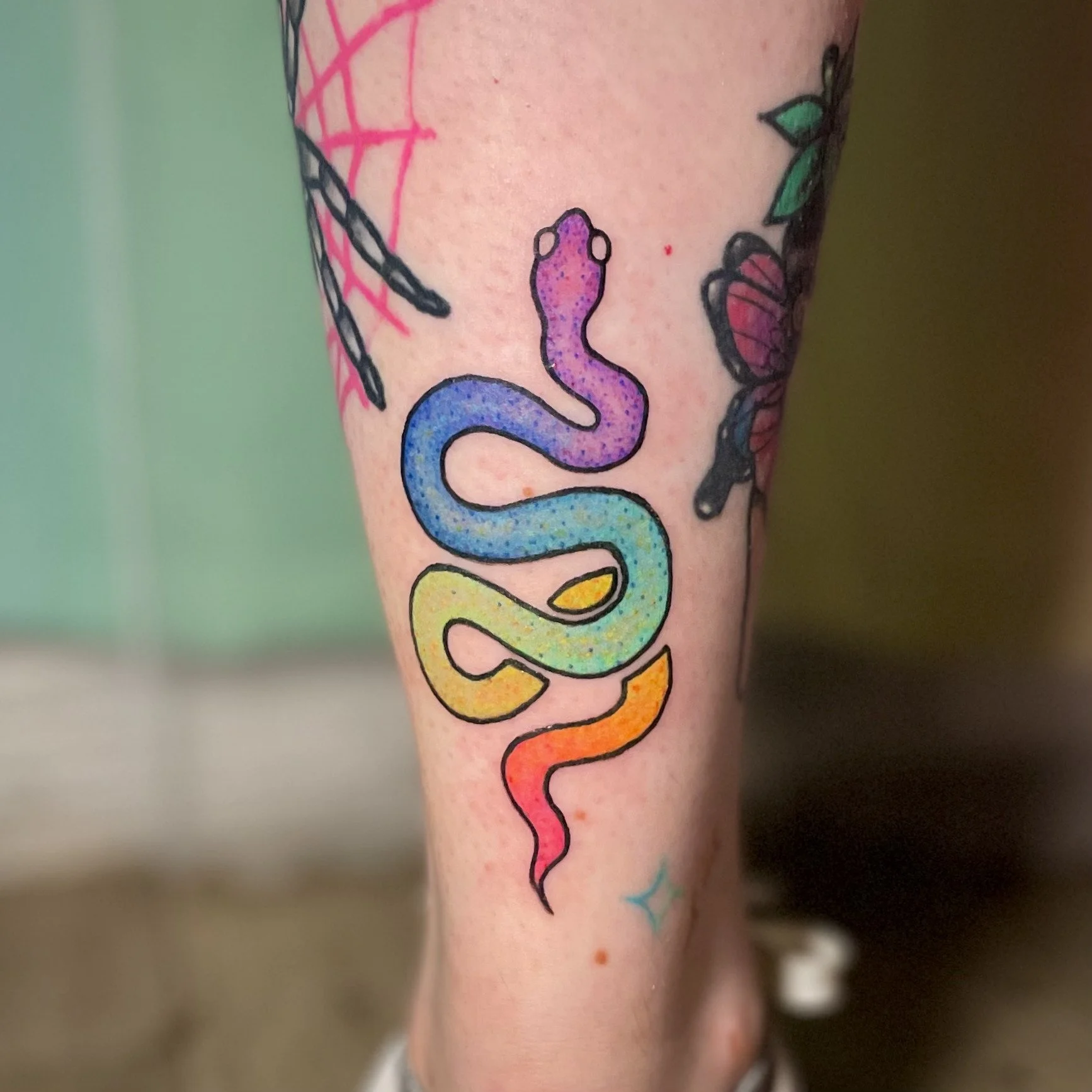 Colorful rainbow snake tattoo on person's leg.