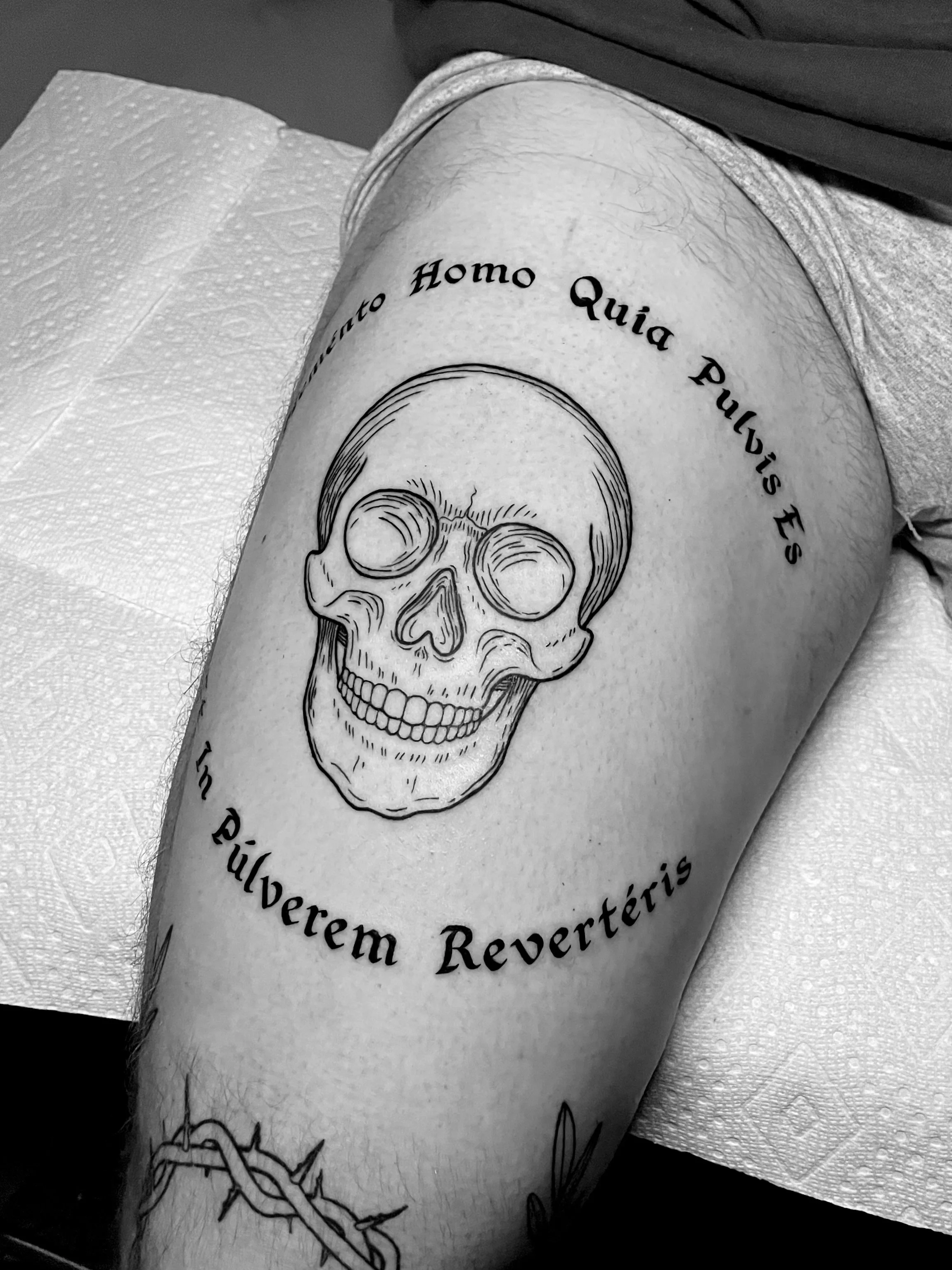 Tattoo of a human skull with Latin text around it on a person's upper arm.
