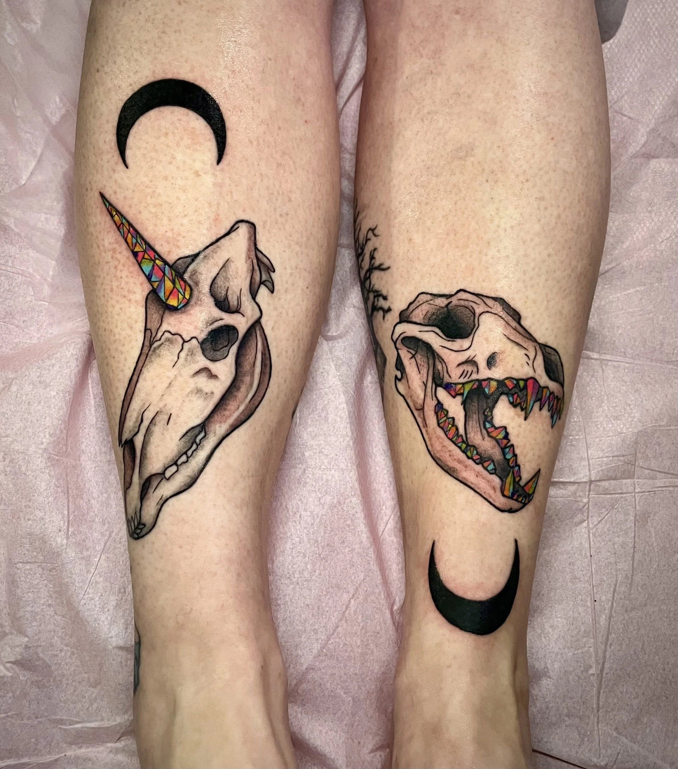 Tattoo of animal skulls with colorful unicorn and dinosaur teeth; crescent moon on left and crescent moon on right.