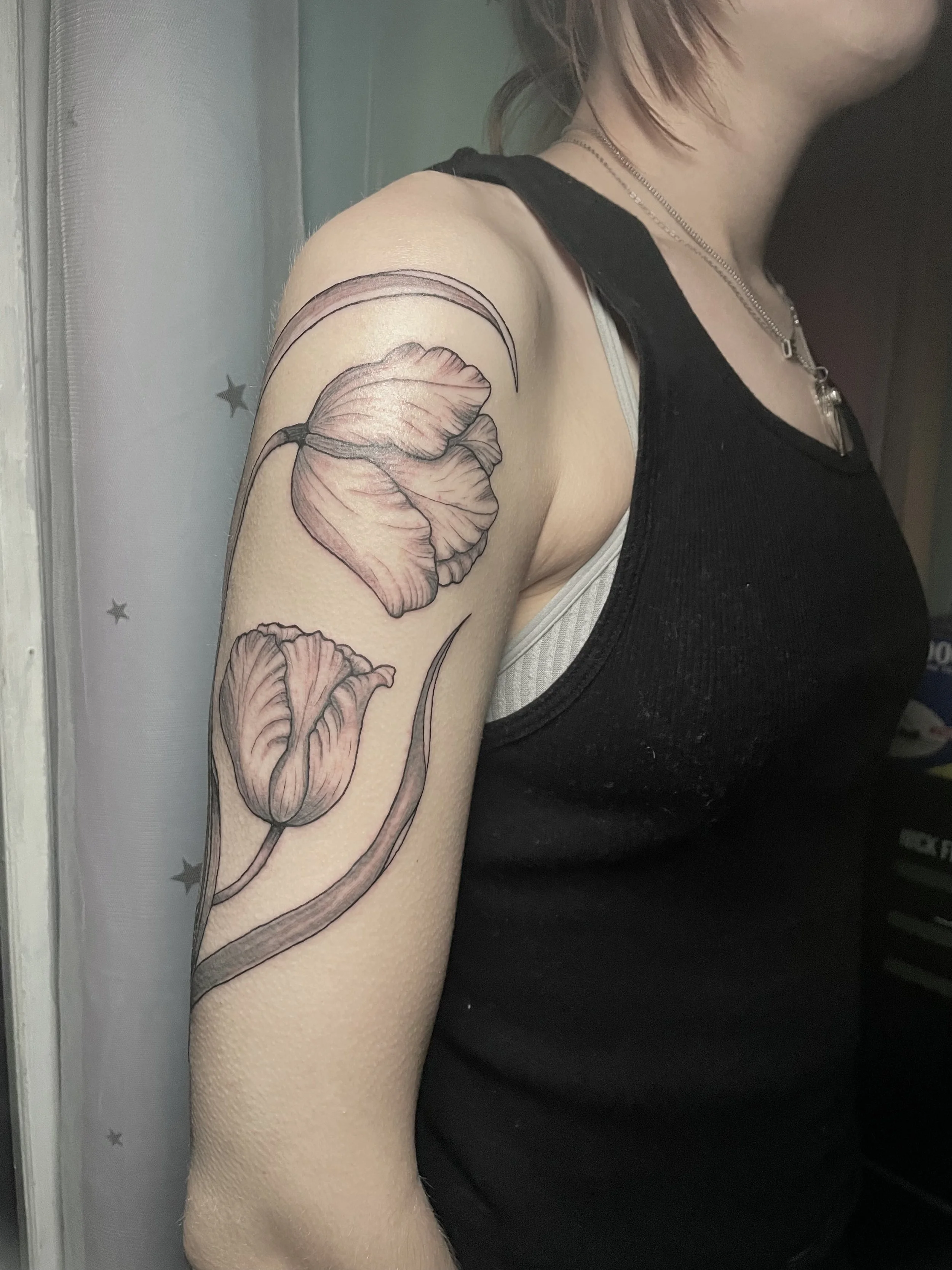 Tattoo of two tulip flowers on the upper arm of a woman wearing a black sleeveless top.