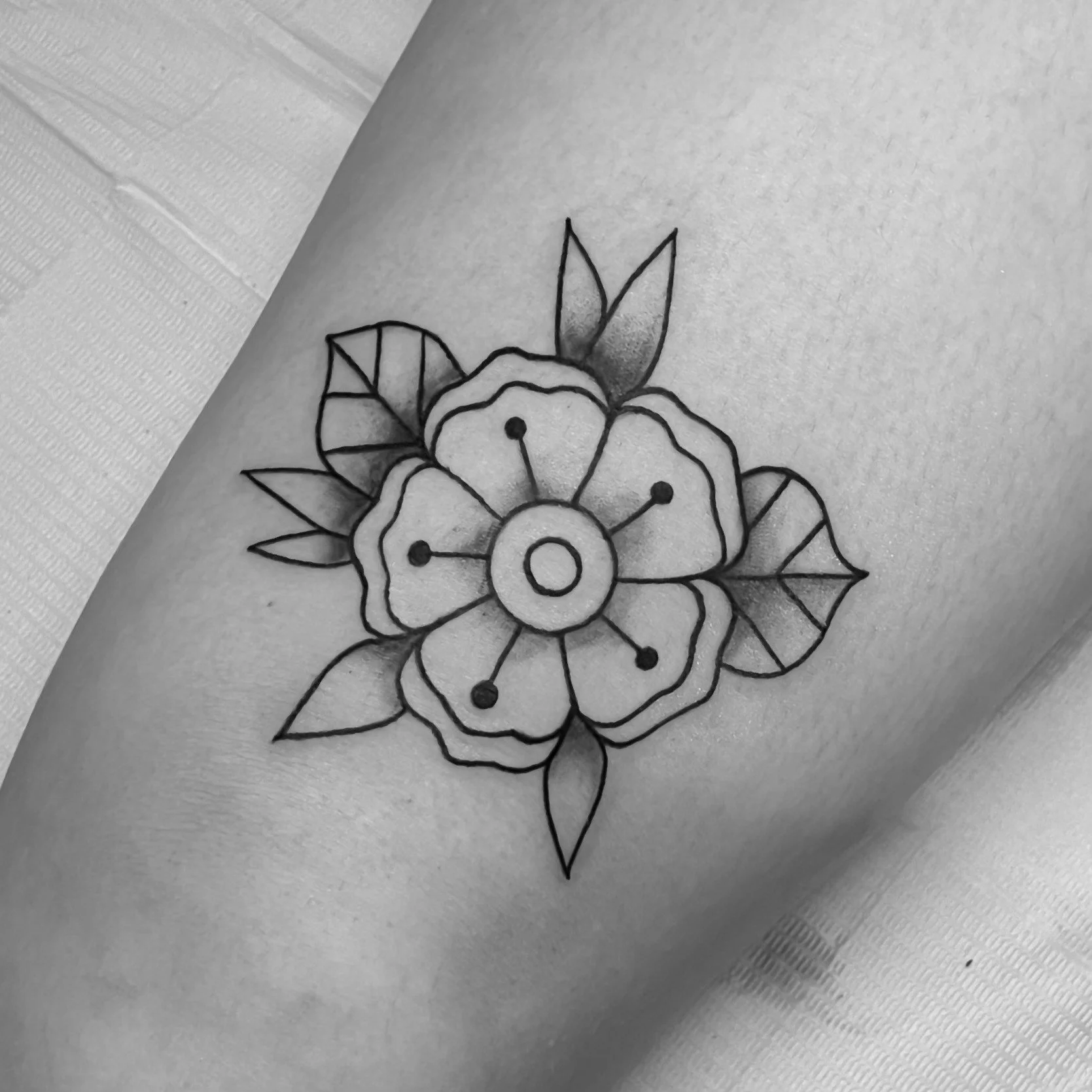 Black and white tattoo of a flower with leaves on person's skin.