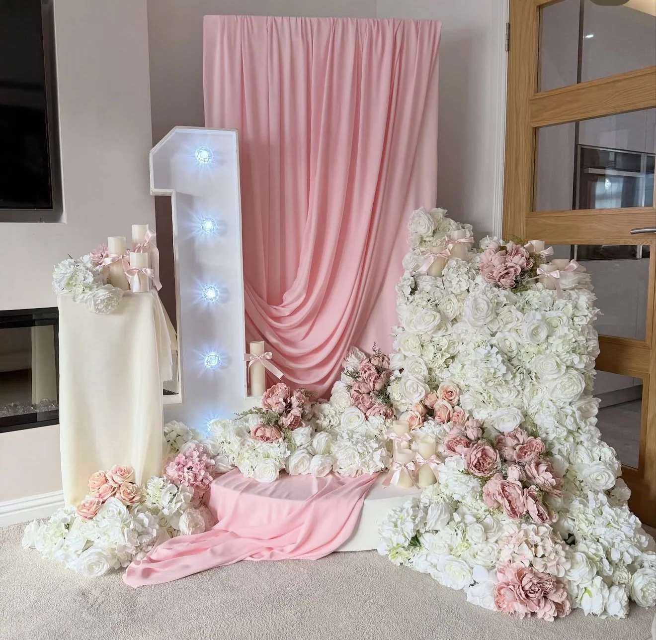 A floral and lighted decorative display with pink and white flowers, candles, and pink fabric backdrop.