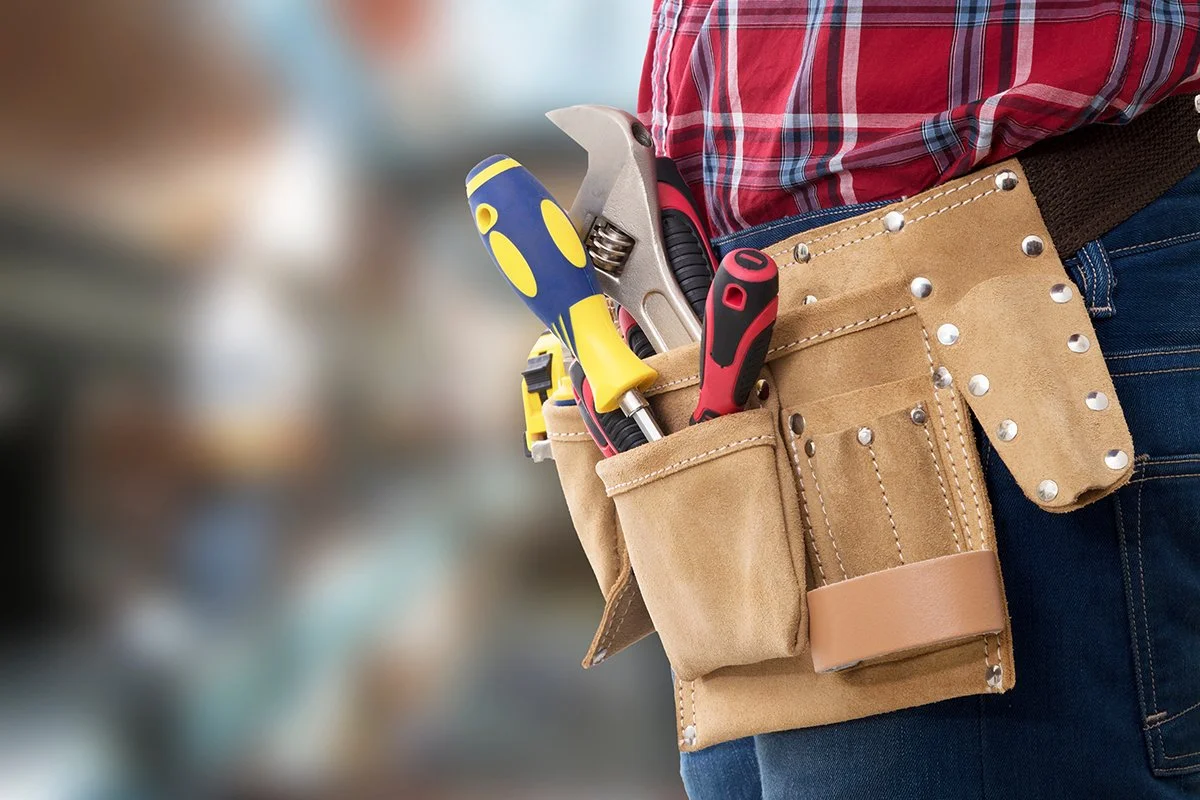 A person wearing a tool belt with screwdrivers, pliers, and a wrench.