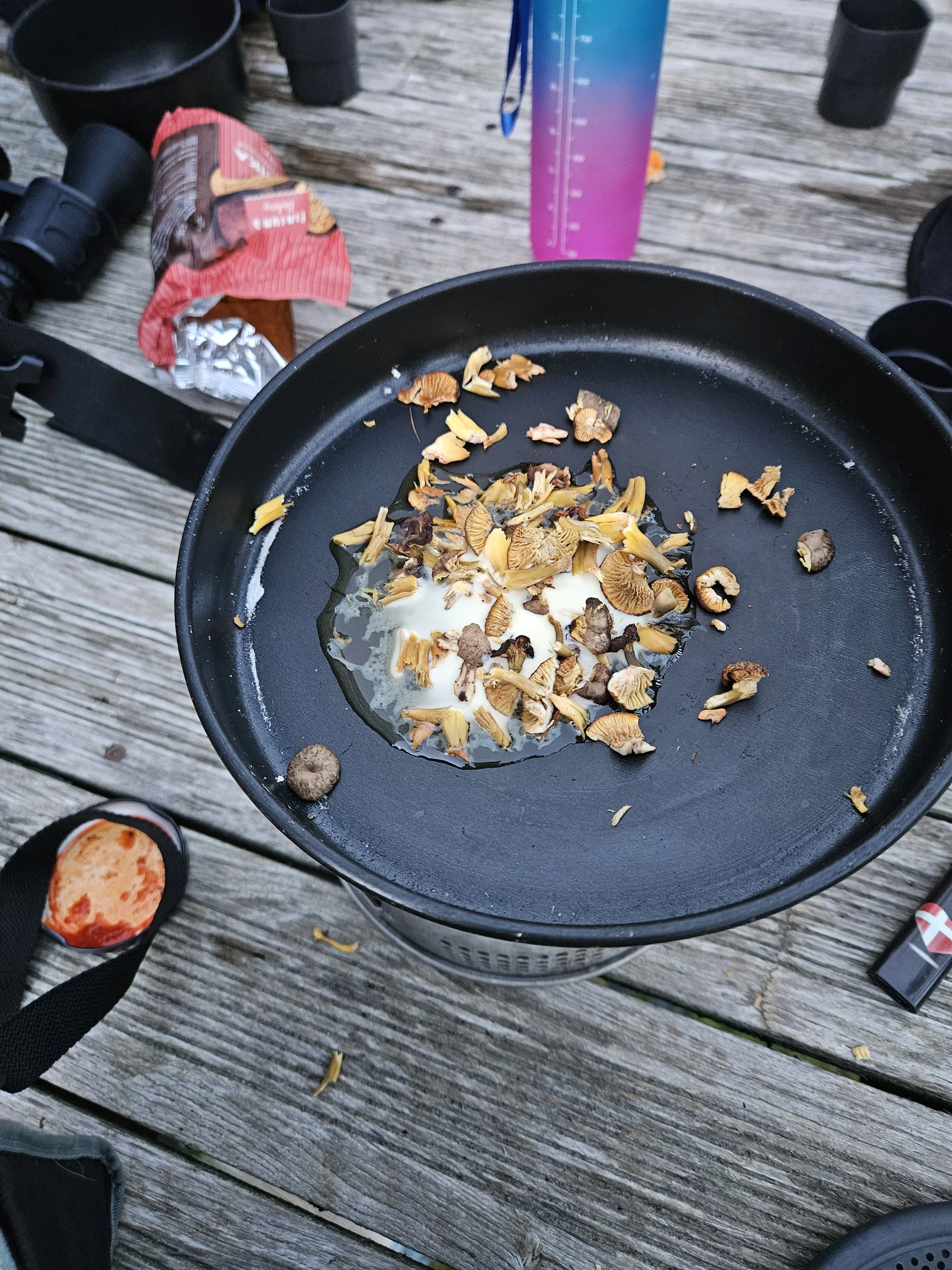 En pande med ristede kantareller og et æg, placeret på et ødelagt træbord udendørs.