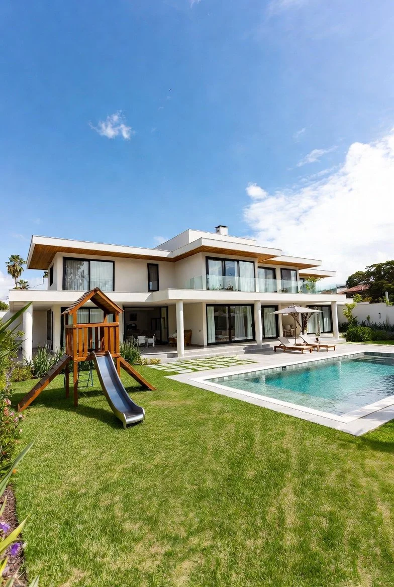 Dein Traumhaus mit großen Glasfenstern, einer Terrasse mit Stühlen und Sonnenschirm, einem Swimmingpool, einem Rutsche für Kinder und einem gepflegten Garten unter einem blauen Himmel.
