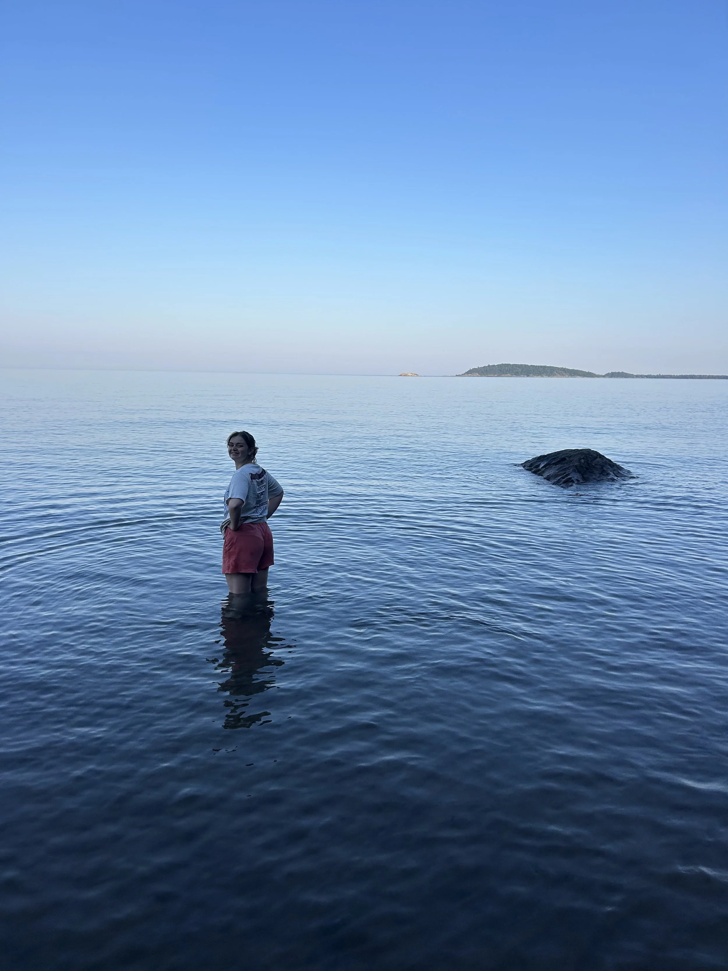 A woman standing knee-deep in water at a beach in Marquette, Michigan.