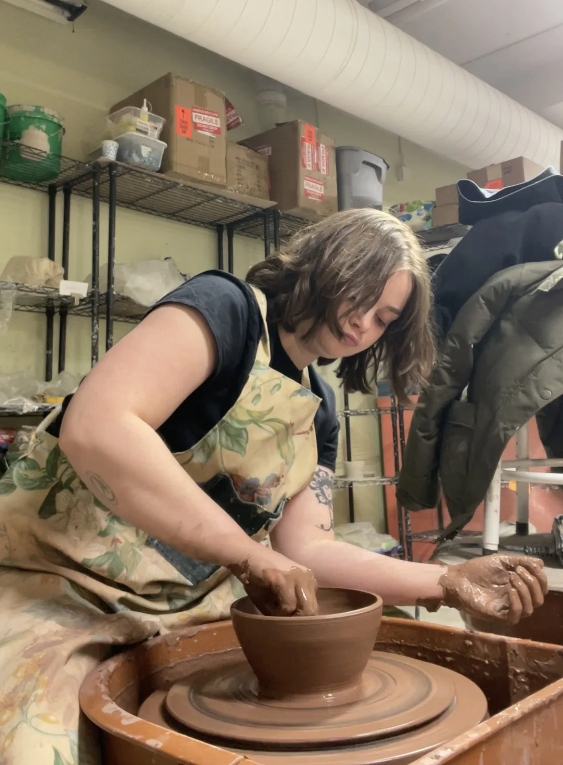 A woman working on a pottery wheel shaping a clay bowl in a ceramic studio.