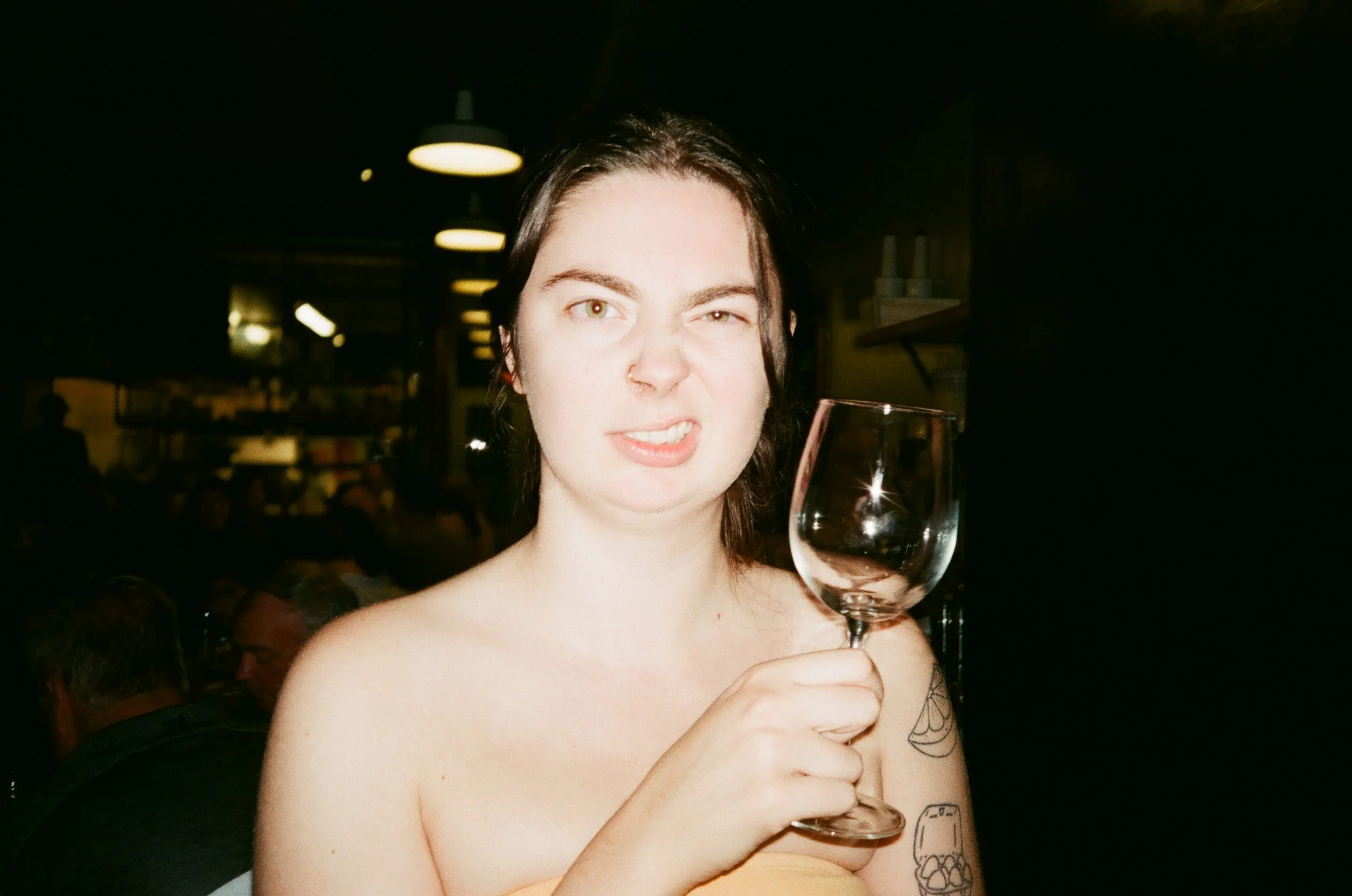 A woman with dark hair holding a wine glass and posing for the camera at a dimly lit restaurant.