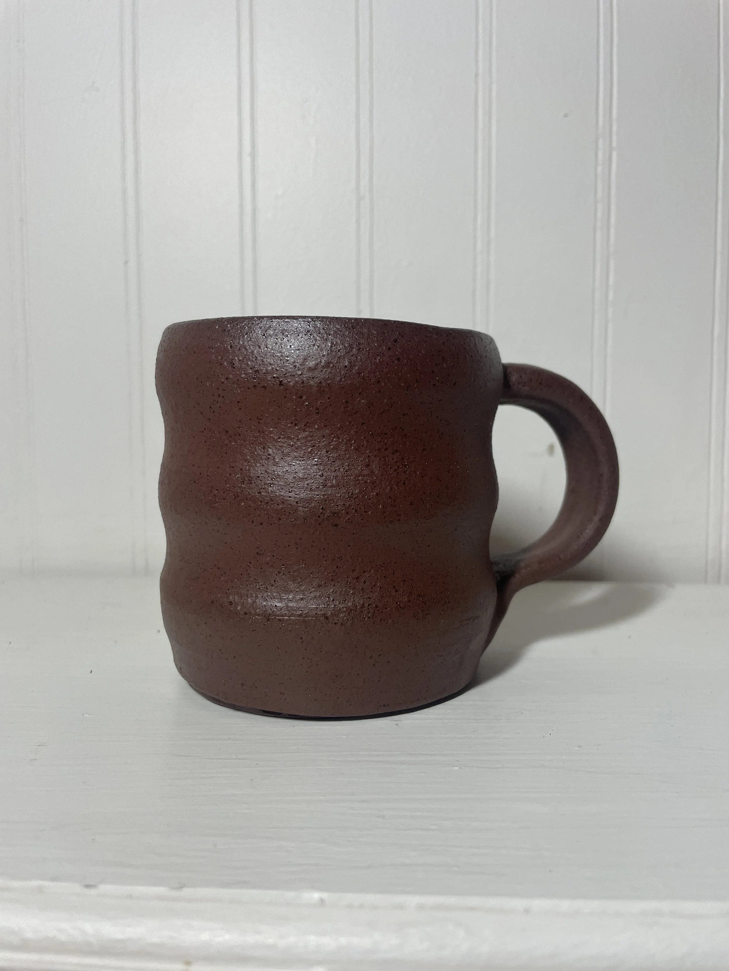 A terra cotta ceramic coffee mug with a wavy profile.