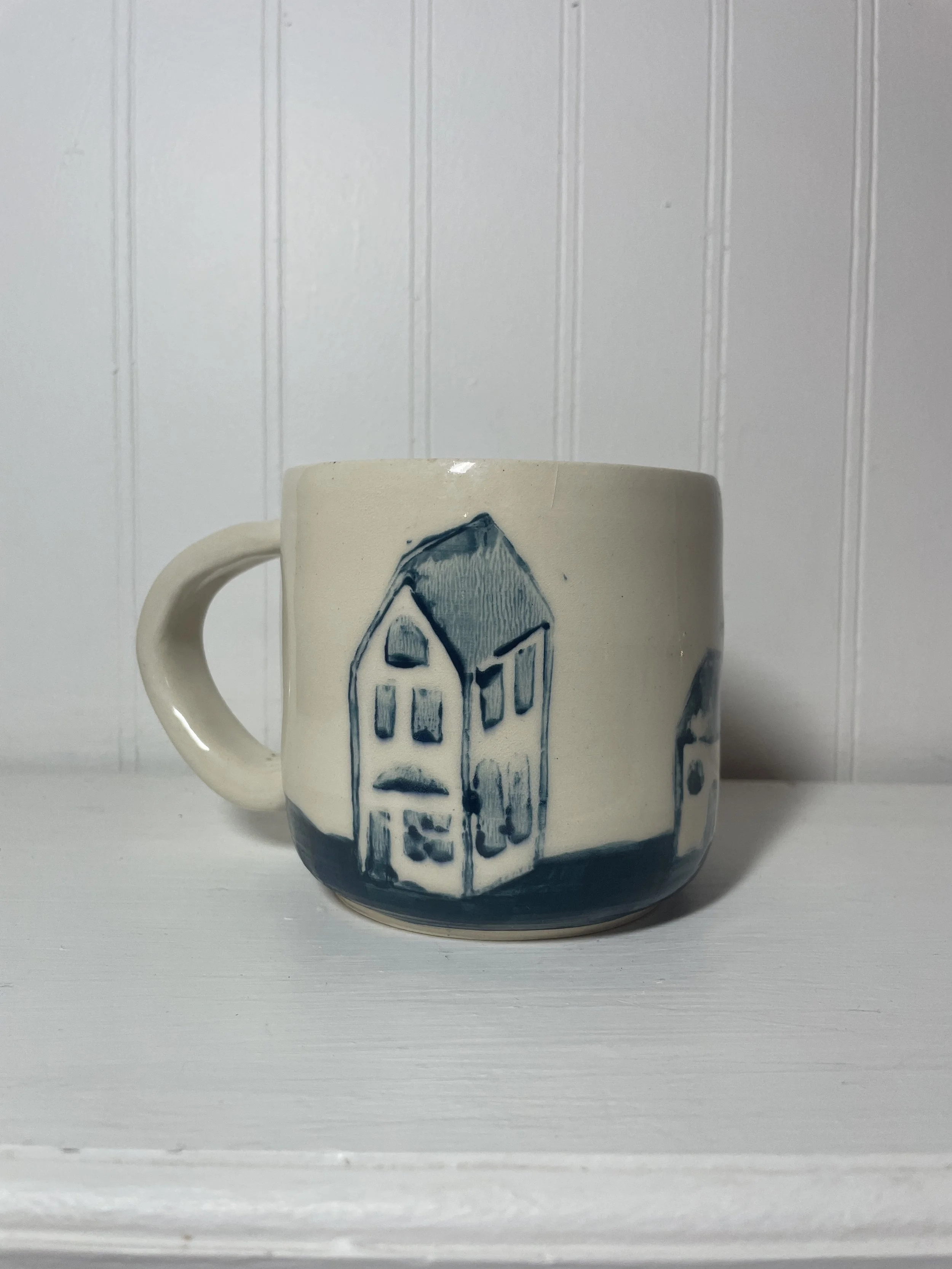 Cream-colored mug with blue linocut-printed house design.