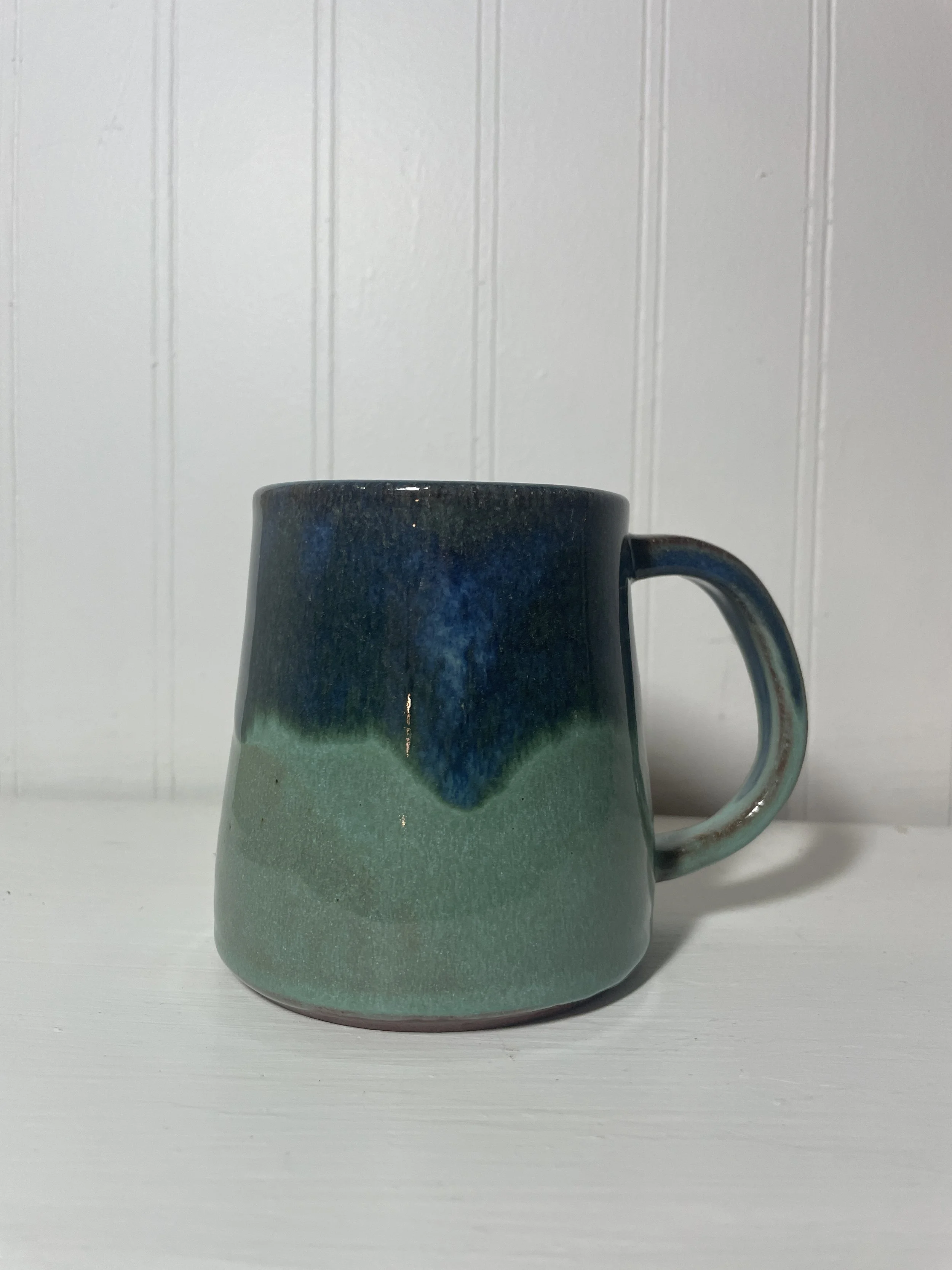 A ceramic coffee mug with gradient glaze from dark blue at the top to teal at the bottom.