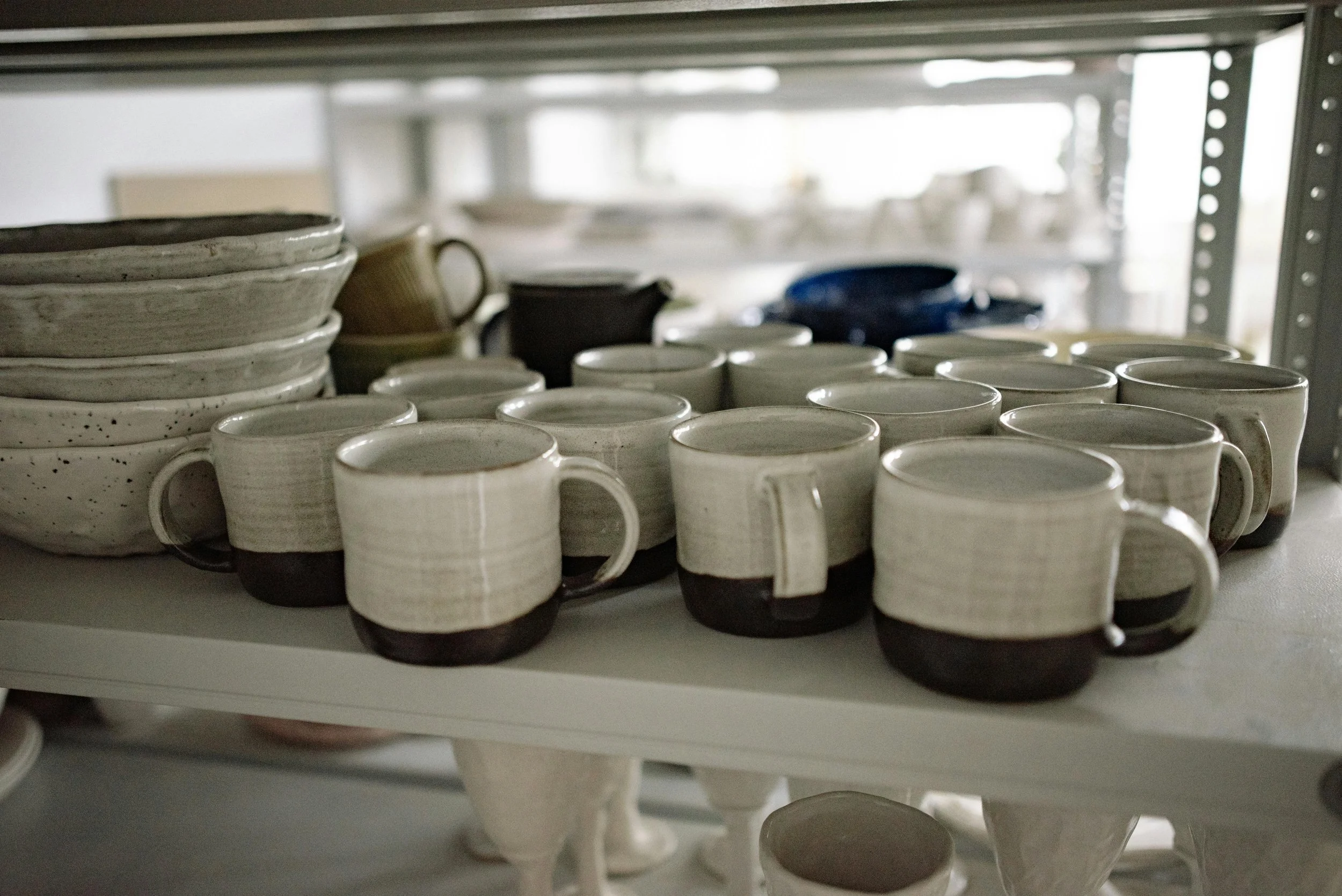 Various handmade ceramic cups and bowls stacked on a shelving unit.