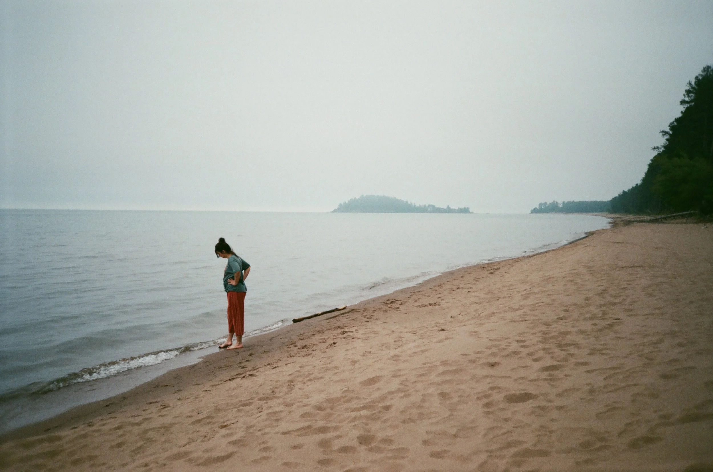 A woman standing on a sandy beach in Marquette, Michigan.