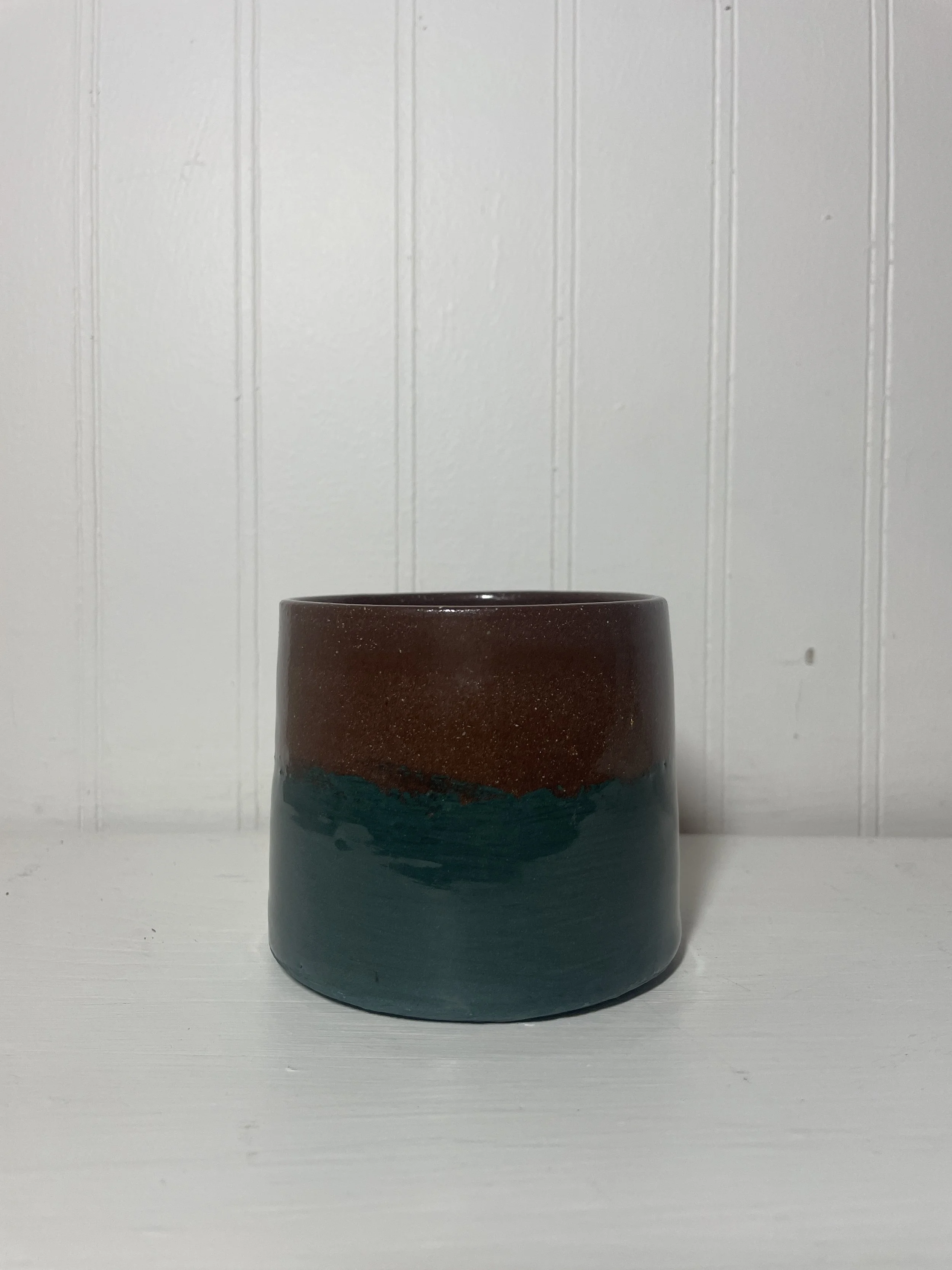A small ceramic cup with a raw terra cotta upper half and a teal lower half.