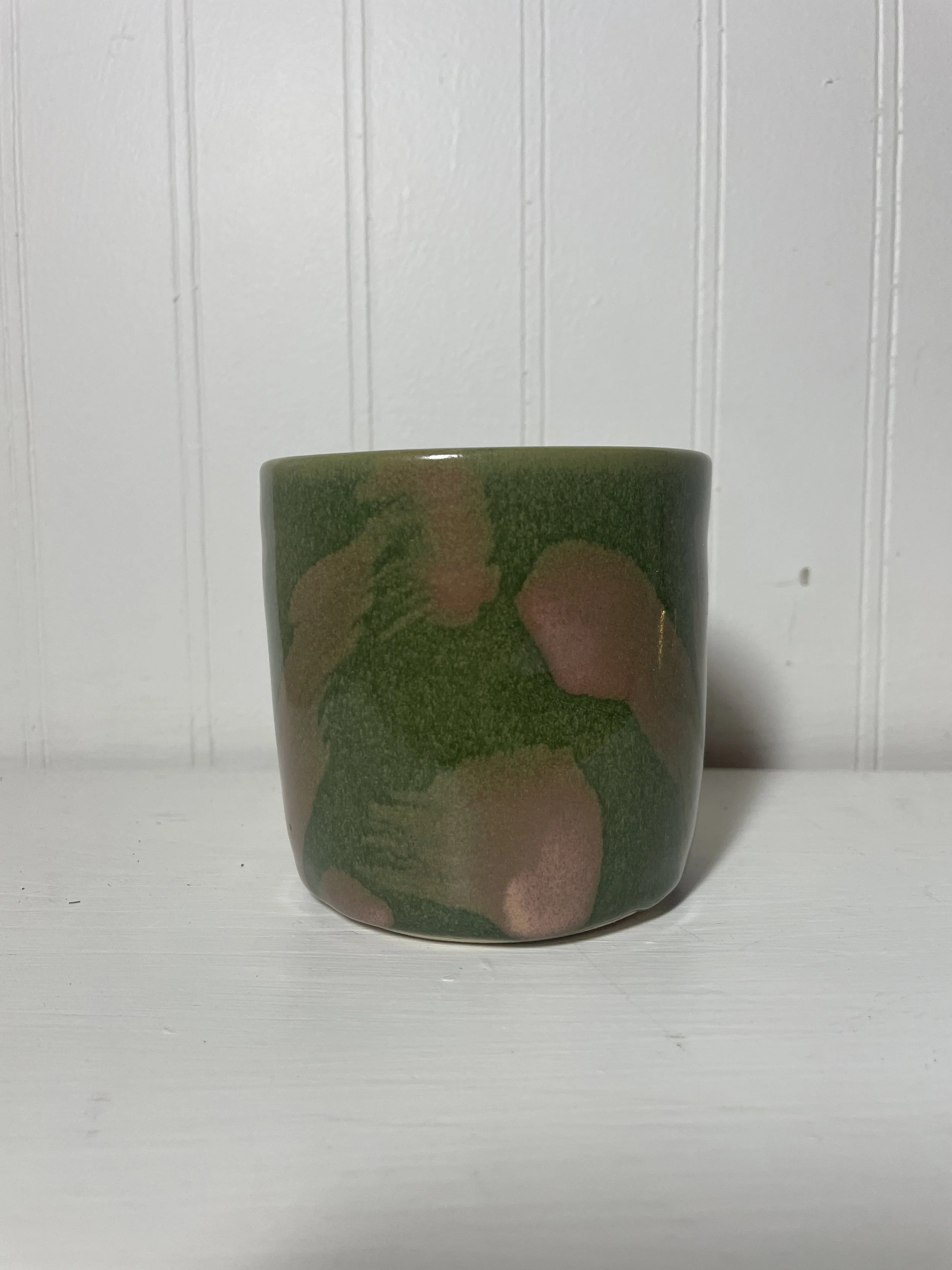A green ceramic mug with pink and tan floral patterns.