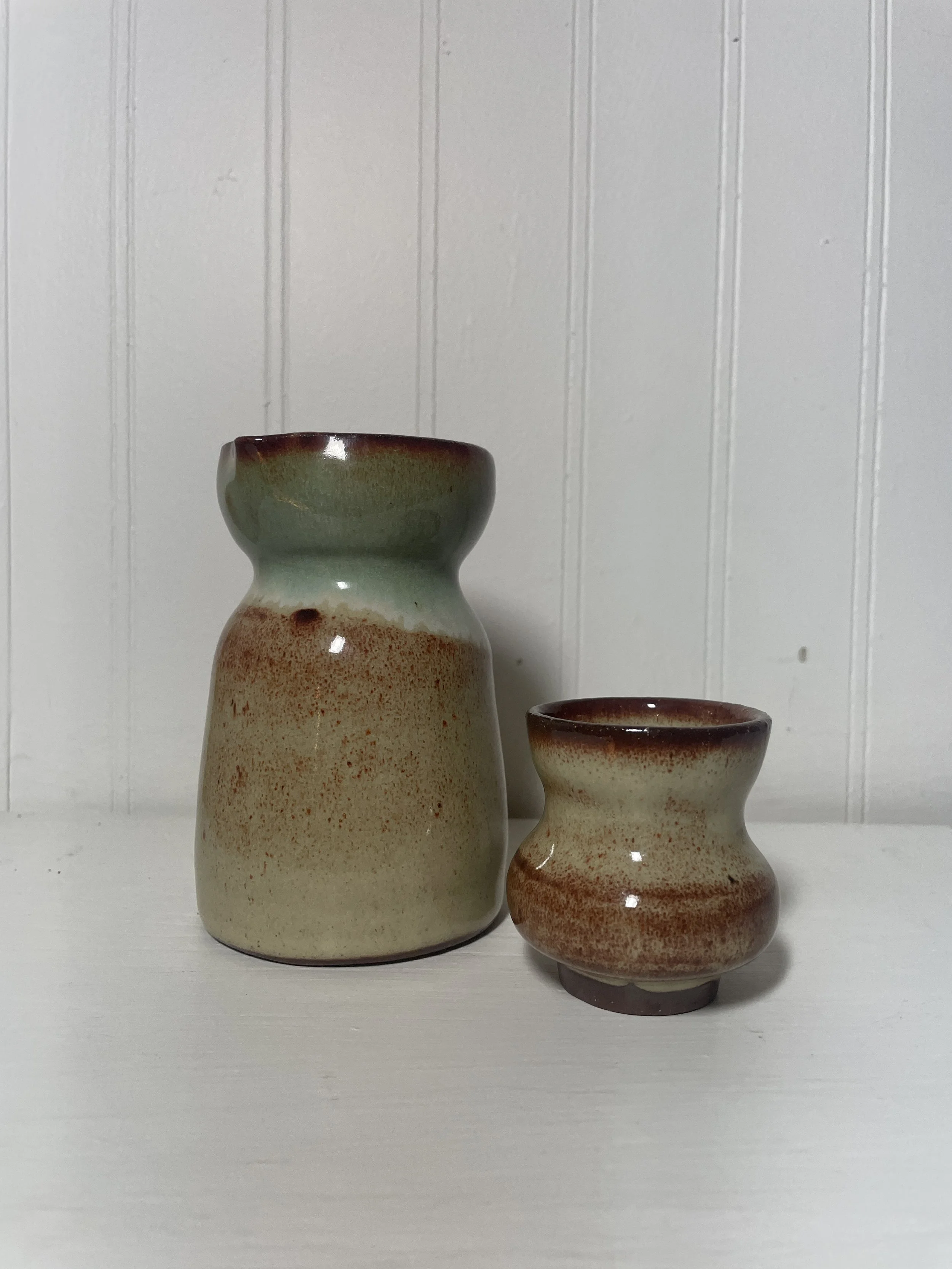 A beige sake set, containing a small sake pitcher and small cup for drinking.
