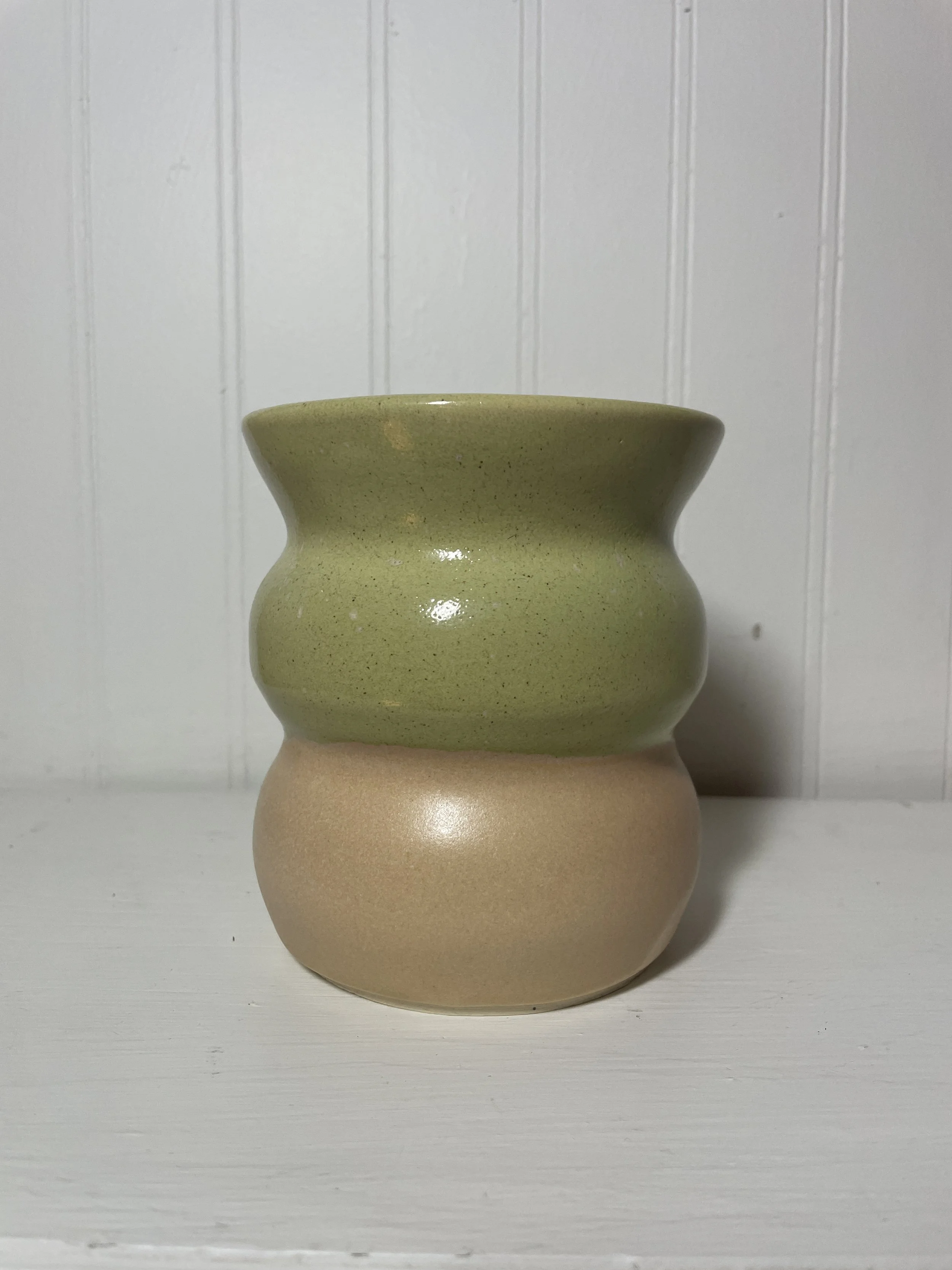 A two-tone, wavy ceramic vase with a green upper section and a beige lower section.