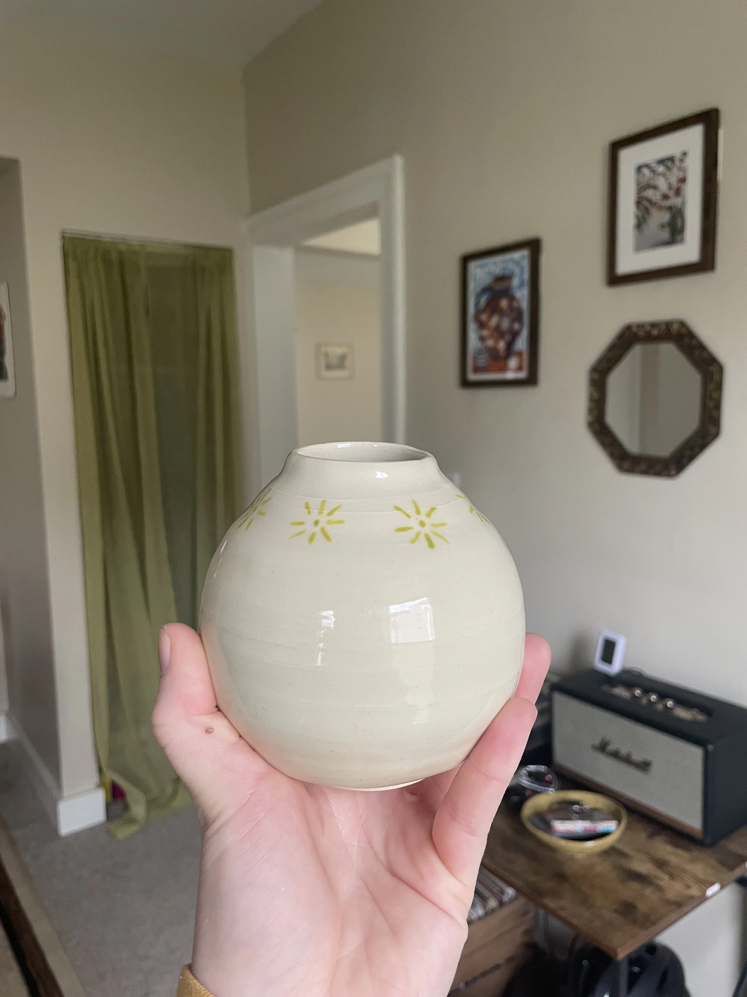 A small beige ceramic vase with a chartreuse, Scandinavian pattern around the top.