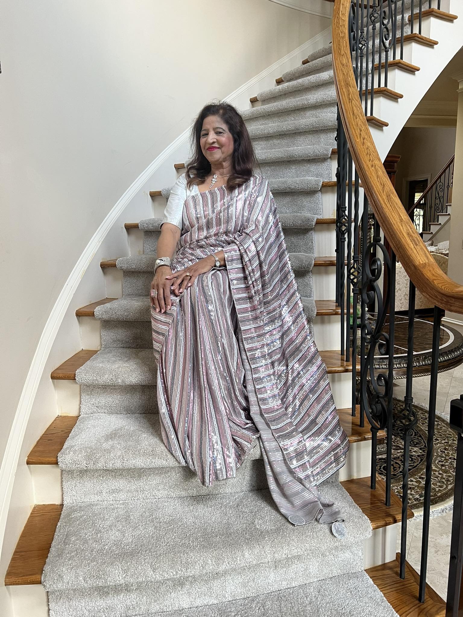 A woman wearing a silver and pink saree sitting on a staircase indoors