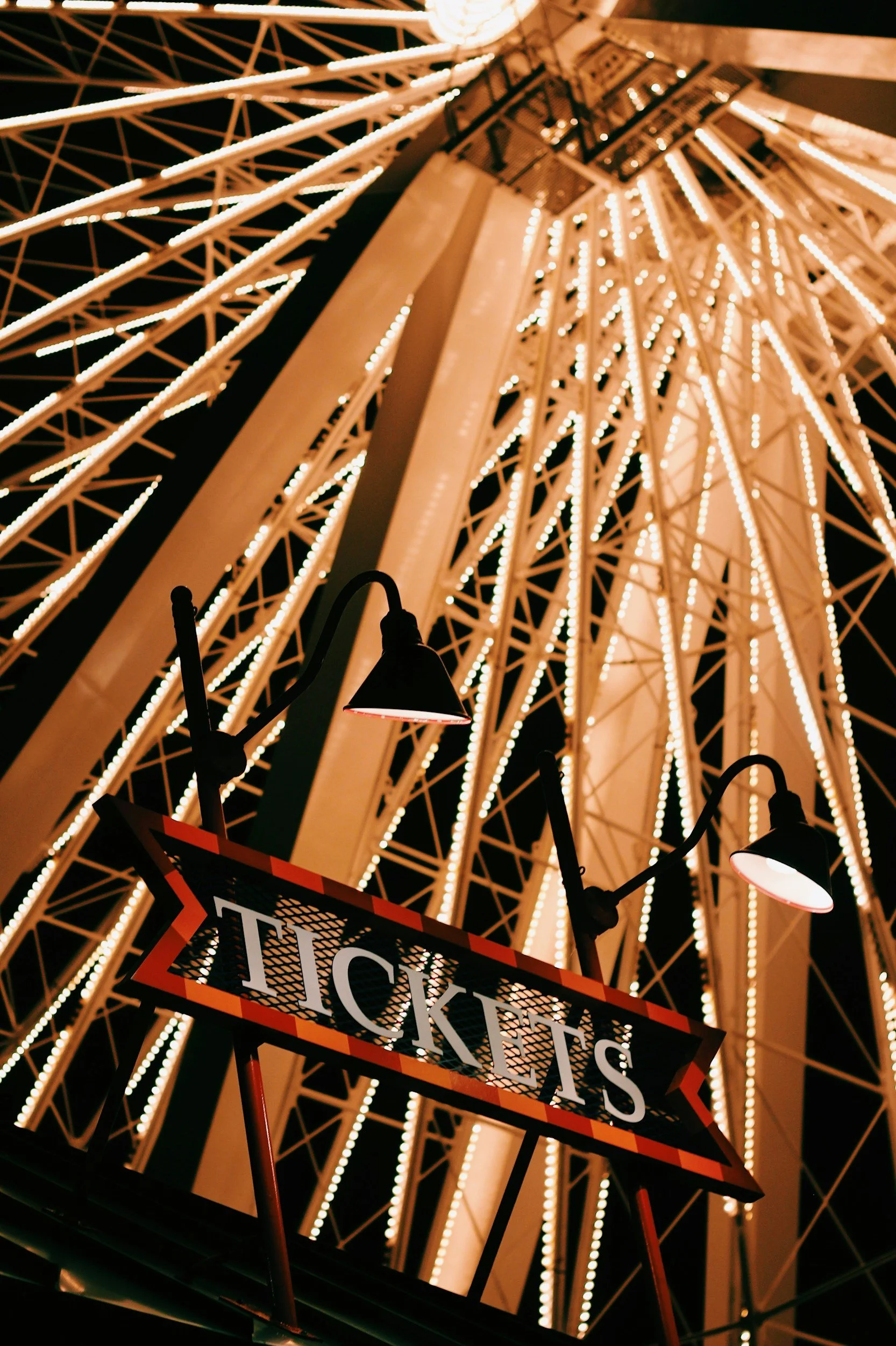 Nighttime view of a lit Ferris wheel with a ticket booth sign in the foreground.