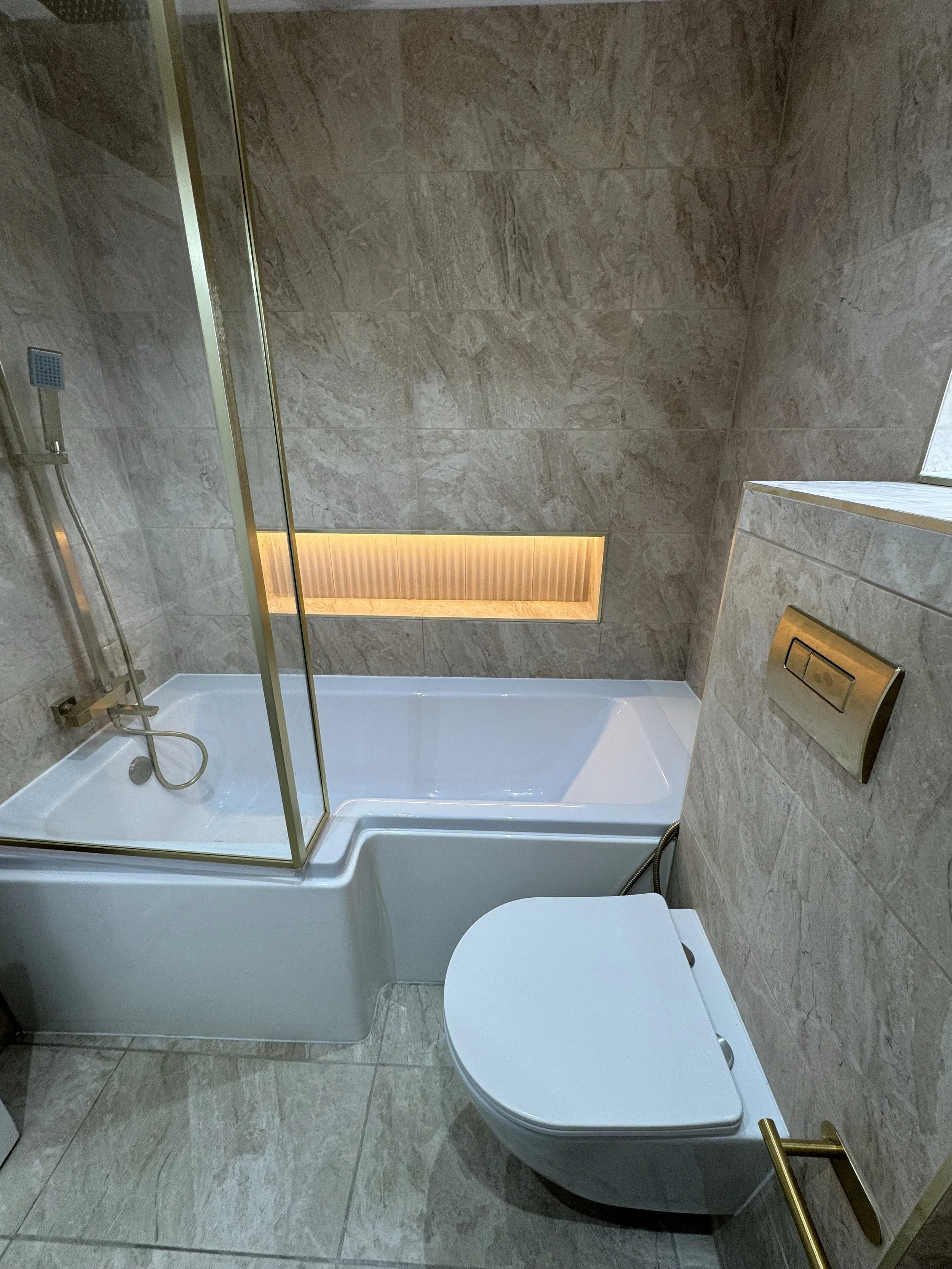Modern bathroom with beige tiled walls and floor, a combined shower and bathtub with glass partition, and a wall-mounted toilet with a concealed flush system.