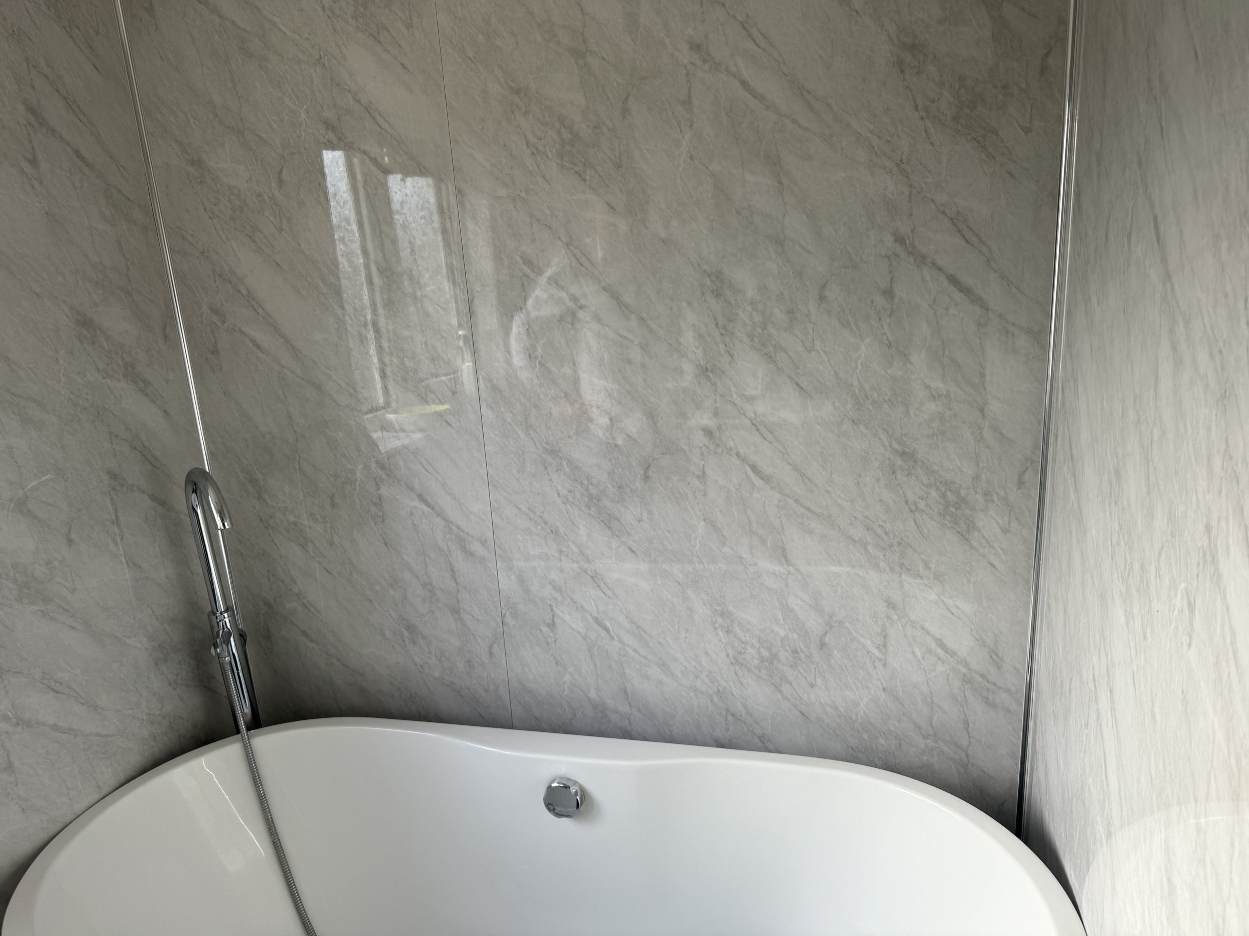 Modern bathroom with a white bathtub, gray marble wall, and a silver handheld showerhead.